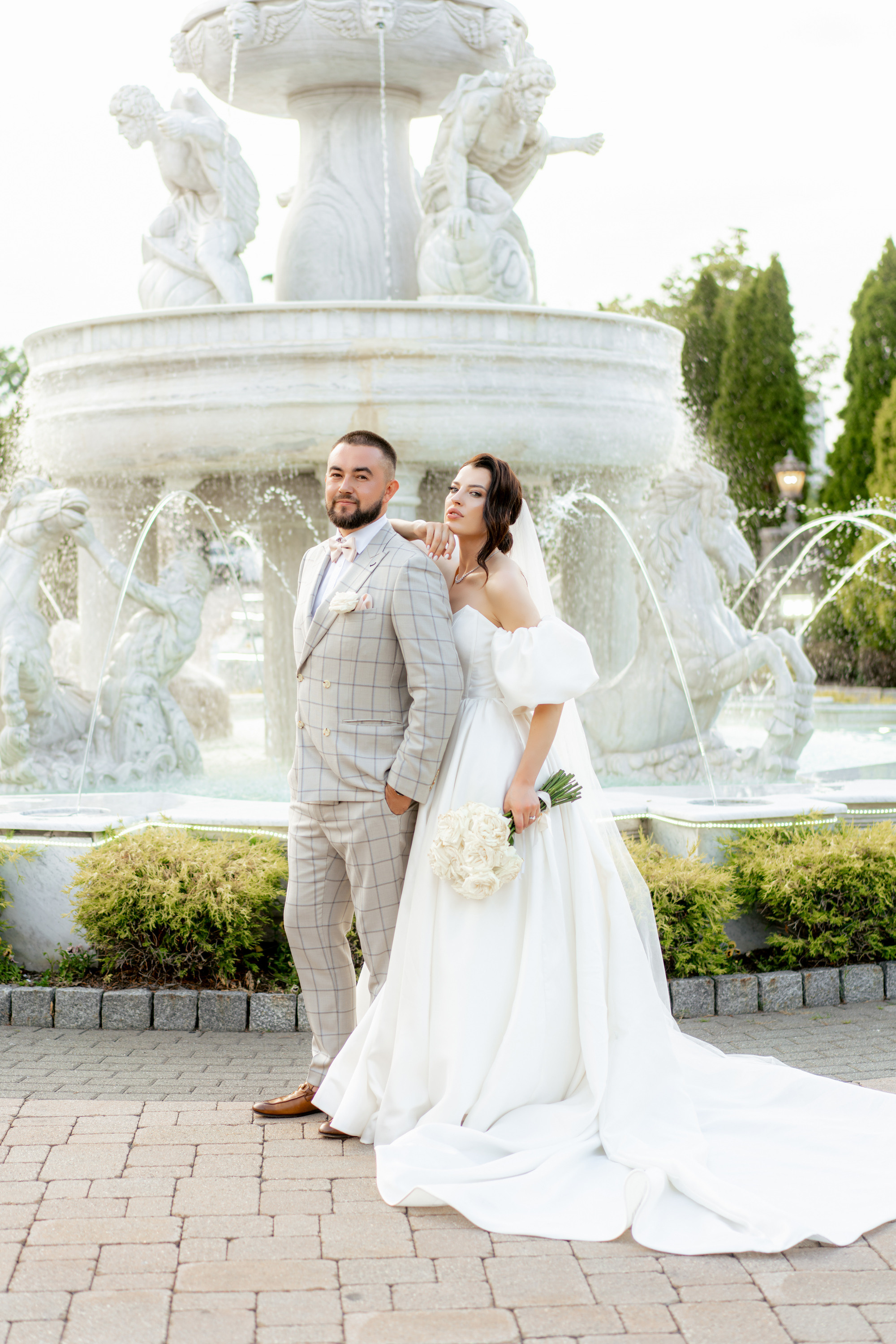 a bride and groom pose in front of a fountain