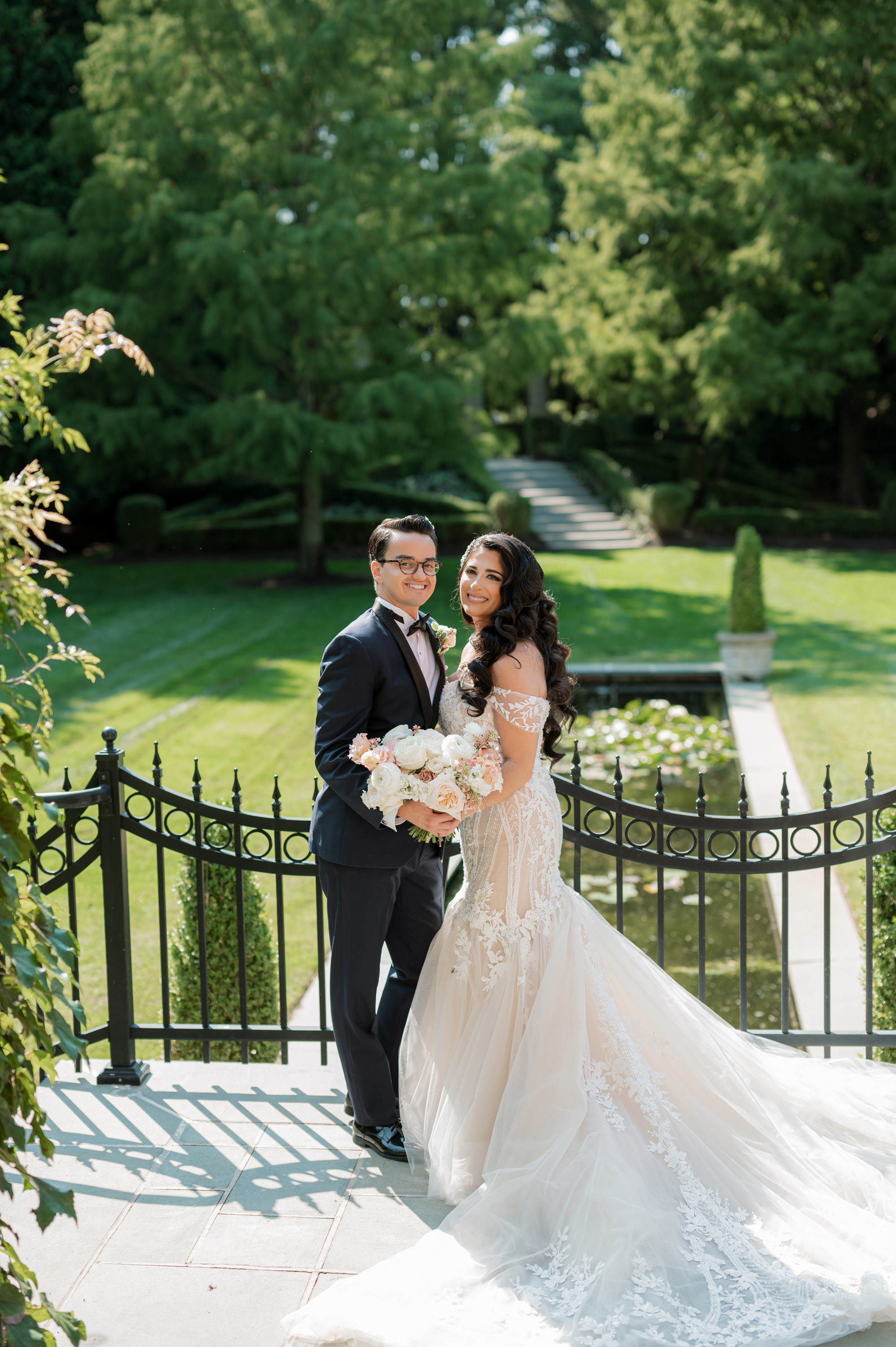 a bride and groom pose for a photo in front of a black iron fence