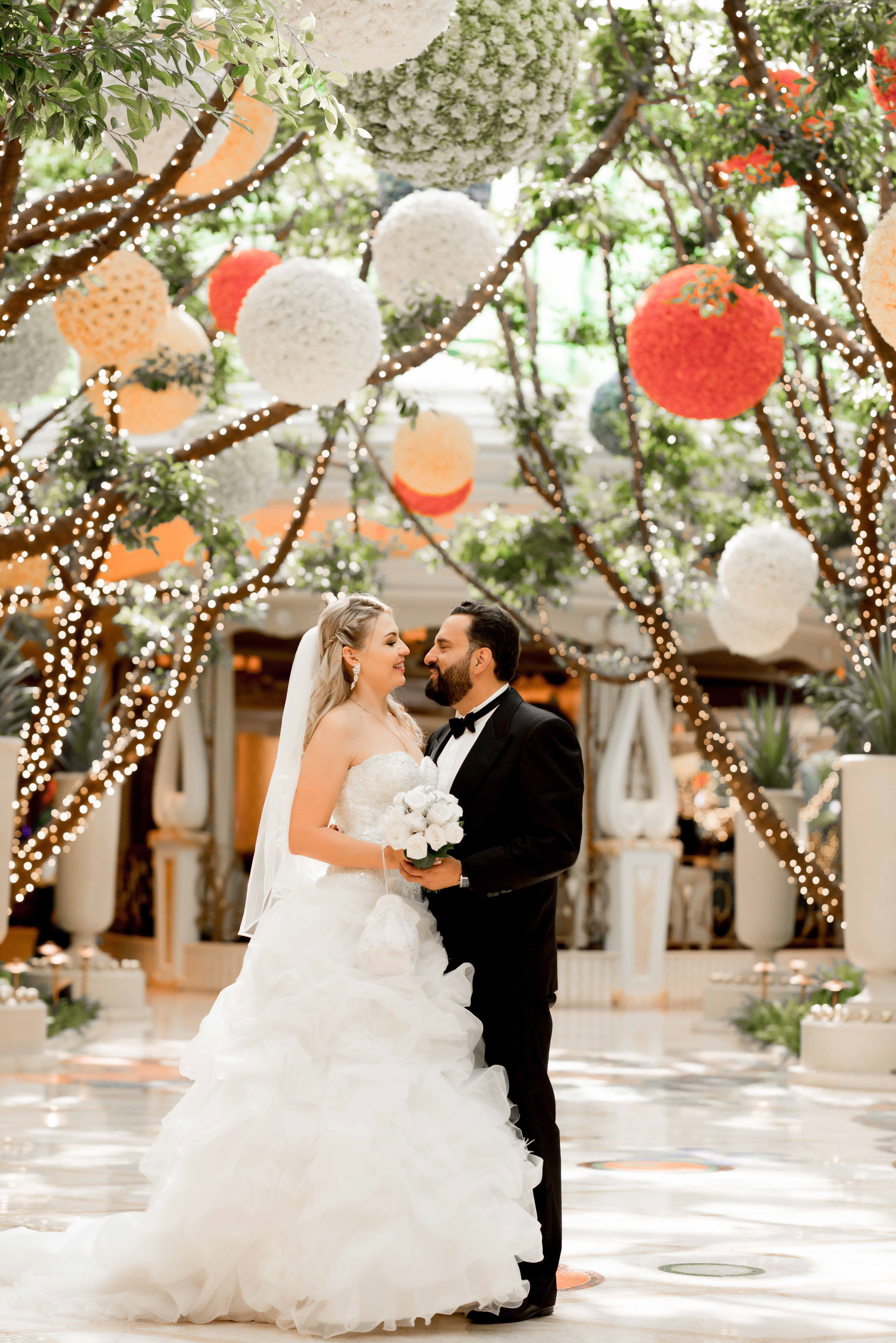 a bride and groom kissing under a canopy of paper lanterns