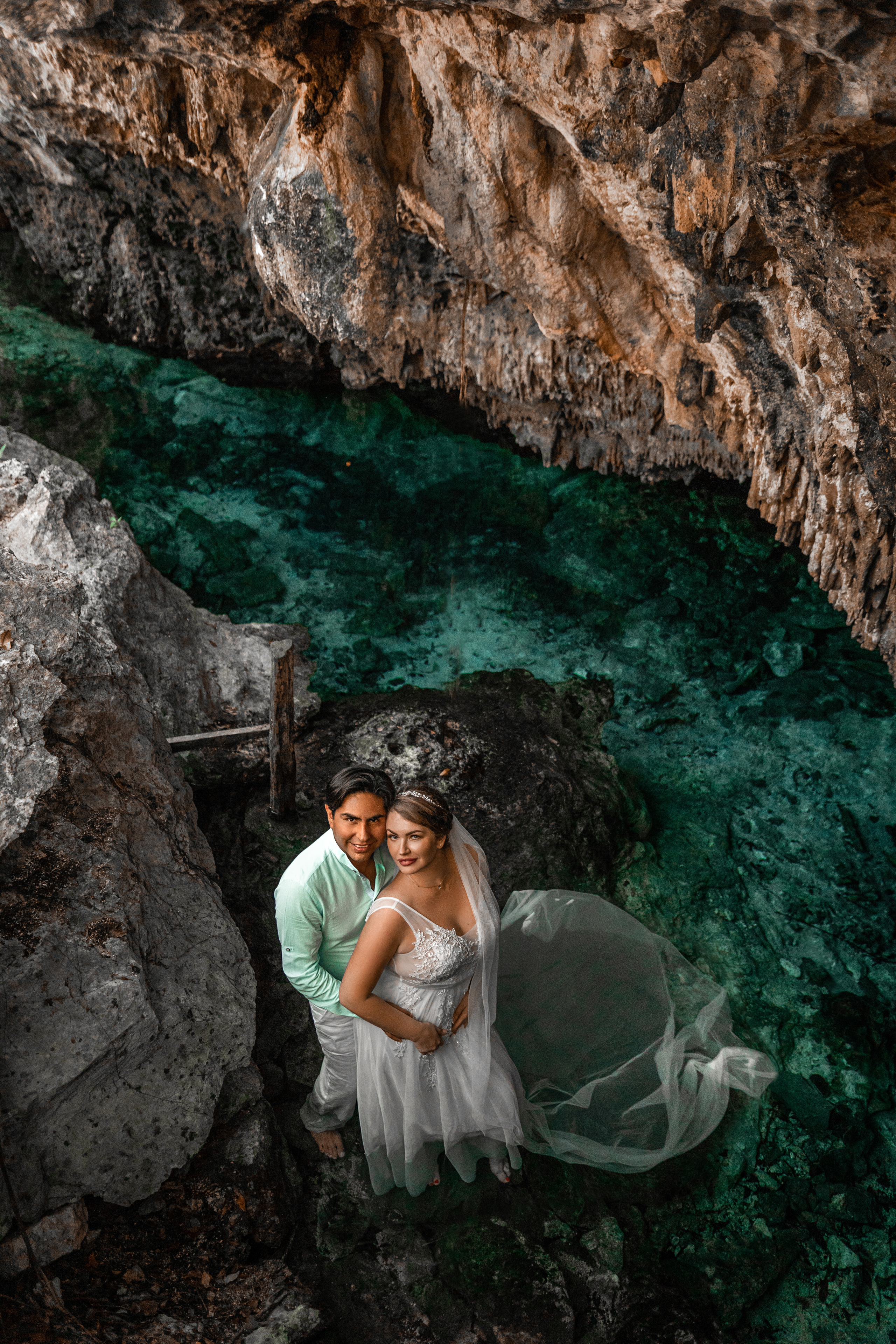 Elegant wedding portrait in jungle cave with crystal-clear water