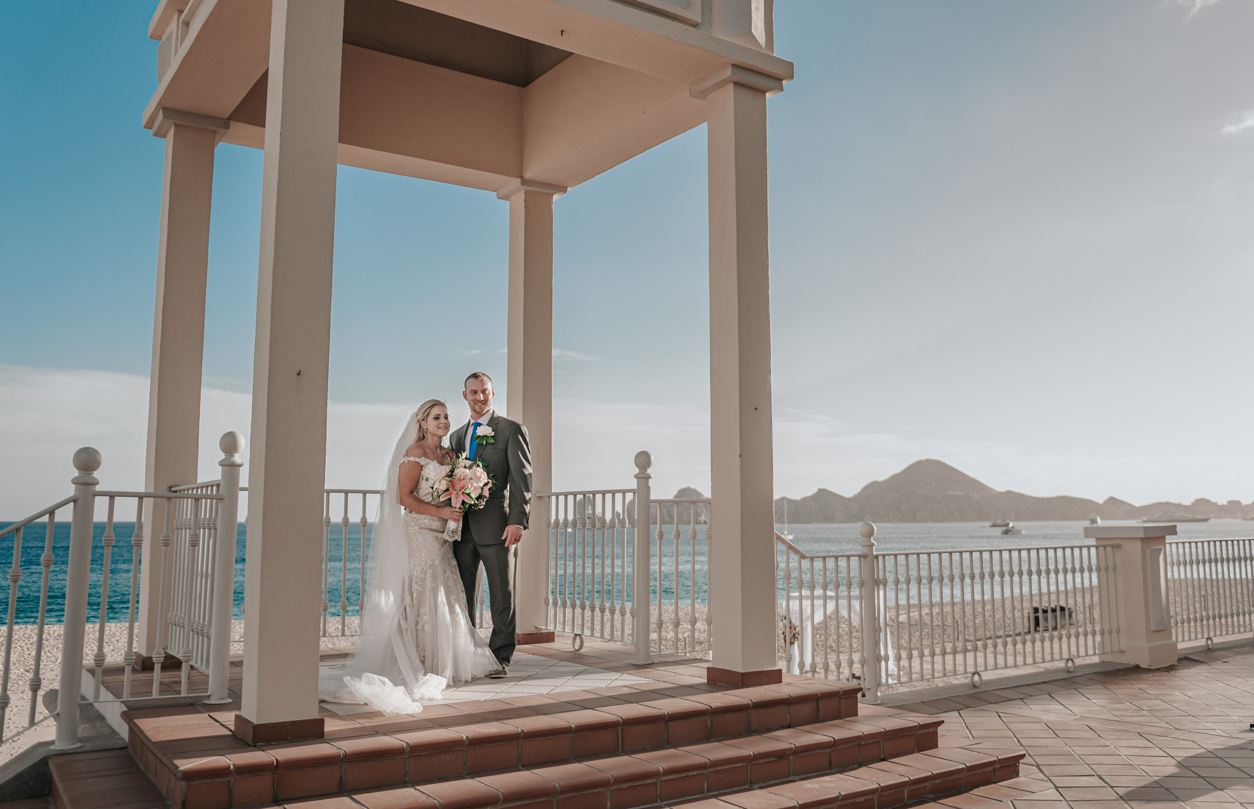 Bride and groom standing under beach gazebo in Cabo San Lucas with scenic mountain view