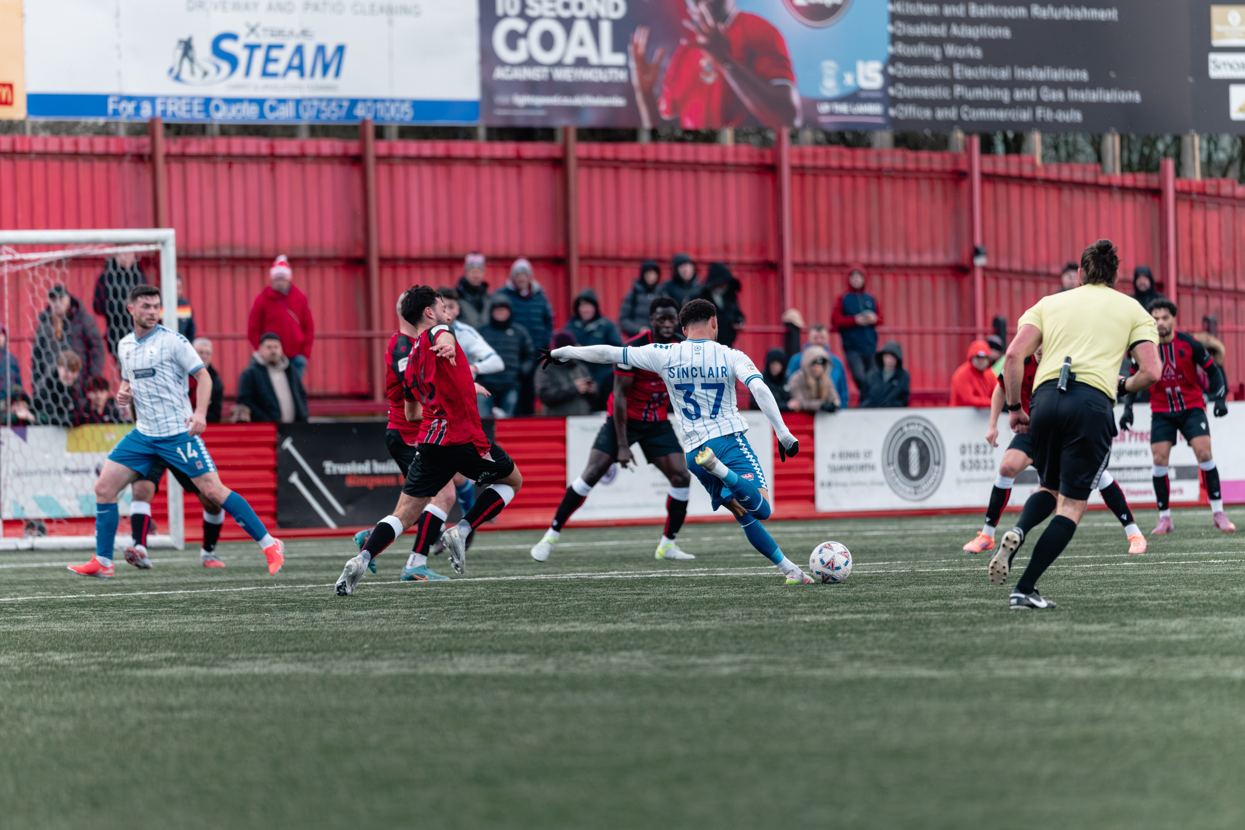 Hartlepool’s No. 37 Sinclair shoots as Tamworth players close him down inside the area at The Lamb Ground.