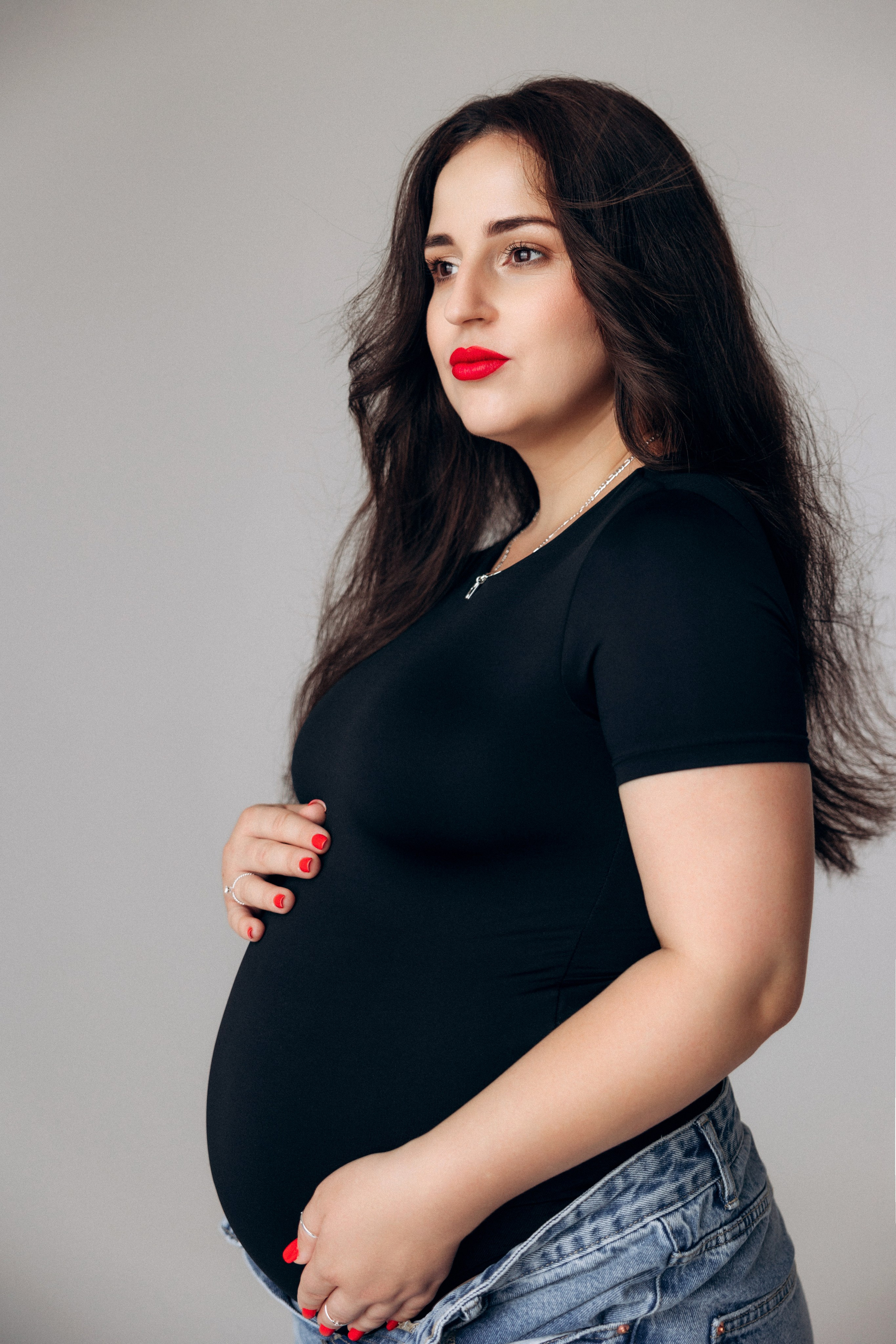 Kobieca fotografia ciążowa – przyszła mama z delikatnym uśmiechem, naturalne światło i prostota.