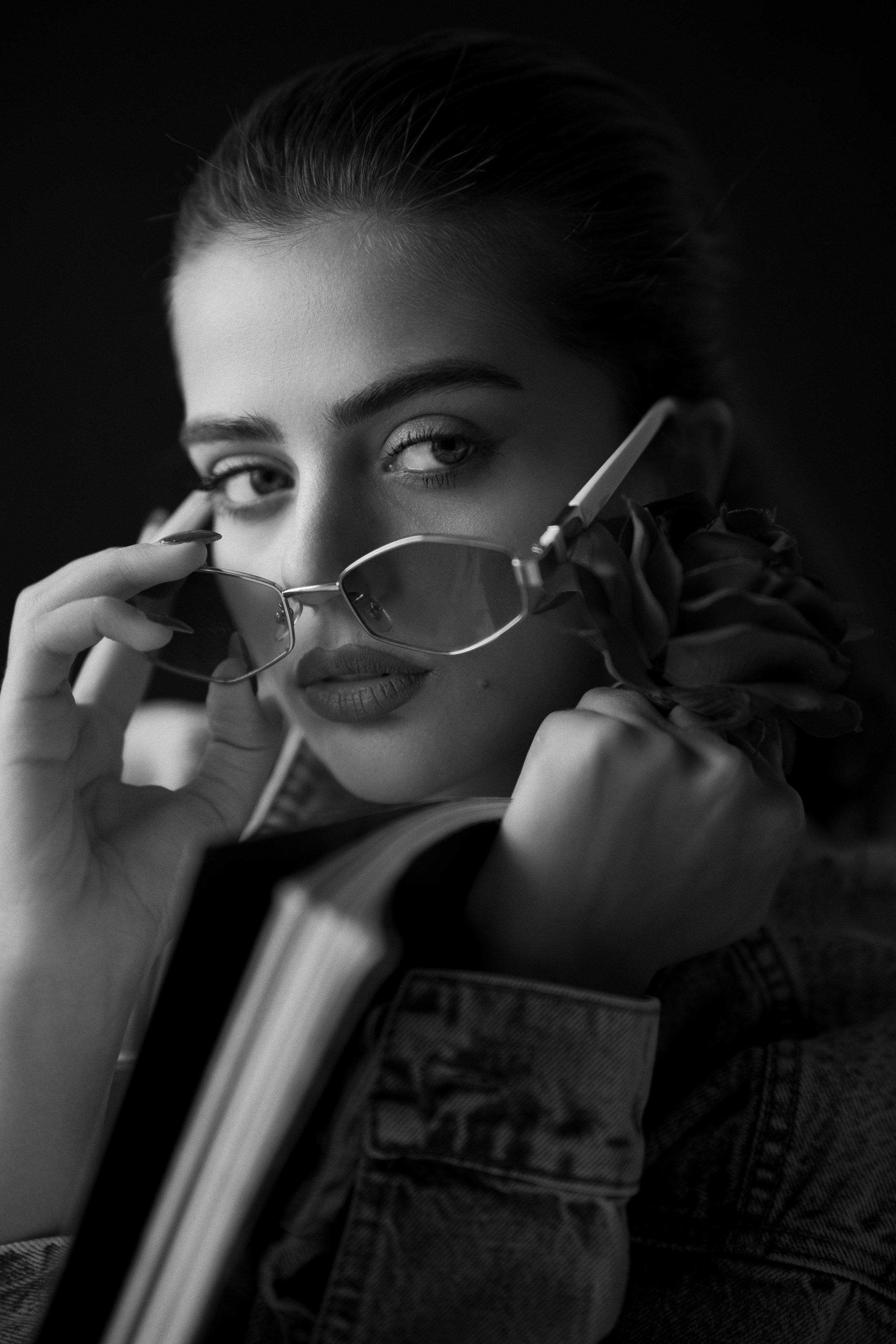 Fashion-inspired black and white female portrait photography by Mehran Hadad featuring a young woman holding sunglasses and a black flower with dramatic fine art studio lighting.