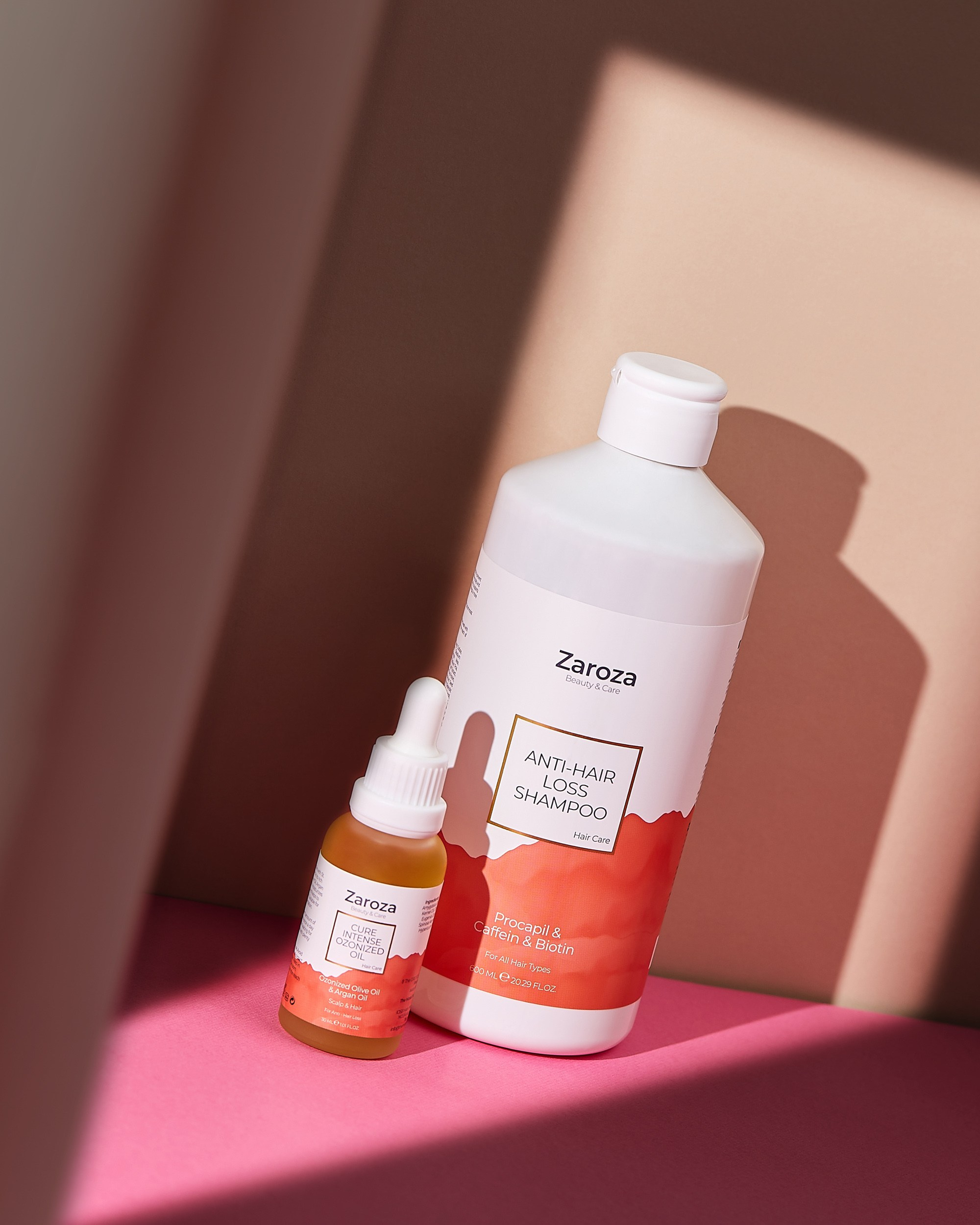 Zarozanın Anti-Hair Loss Shampoo və Cure Intensive Oiled şüşələri, çəhrayı fonda işıq kölgə effektli təqdimat.