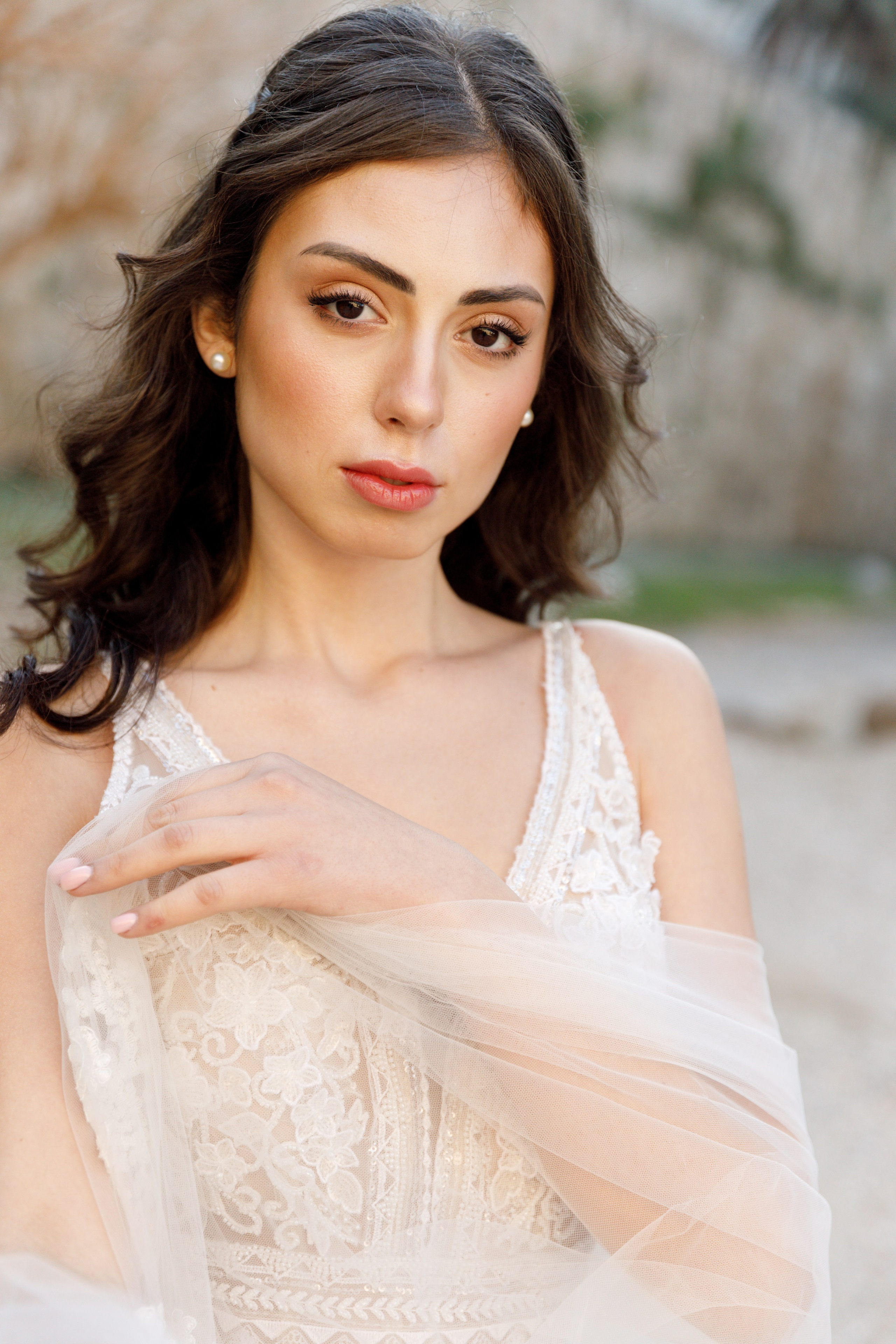 A stunning bride gazes thoughtfully in the enchanting alleys of Rhodes' Old Town, her flowing wedding dress complementing the rustic charm of the cobblestone streets and ancient architecture. The editorial-style portrait captures her poise and the romantic atmosphere of the medieval surroundings, bathed in warm, golden light.