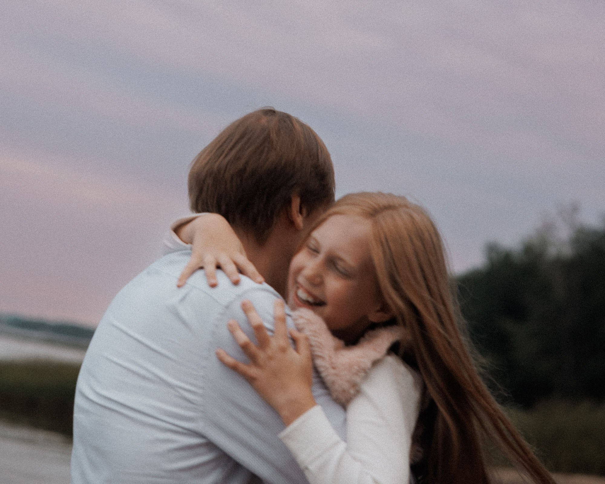 Father hugging his laughing daughter outdoors at dusk