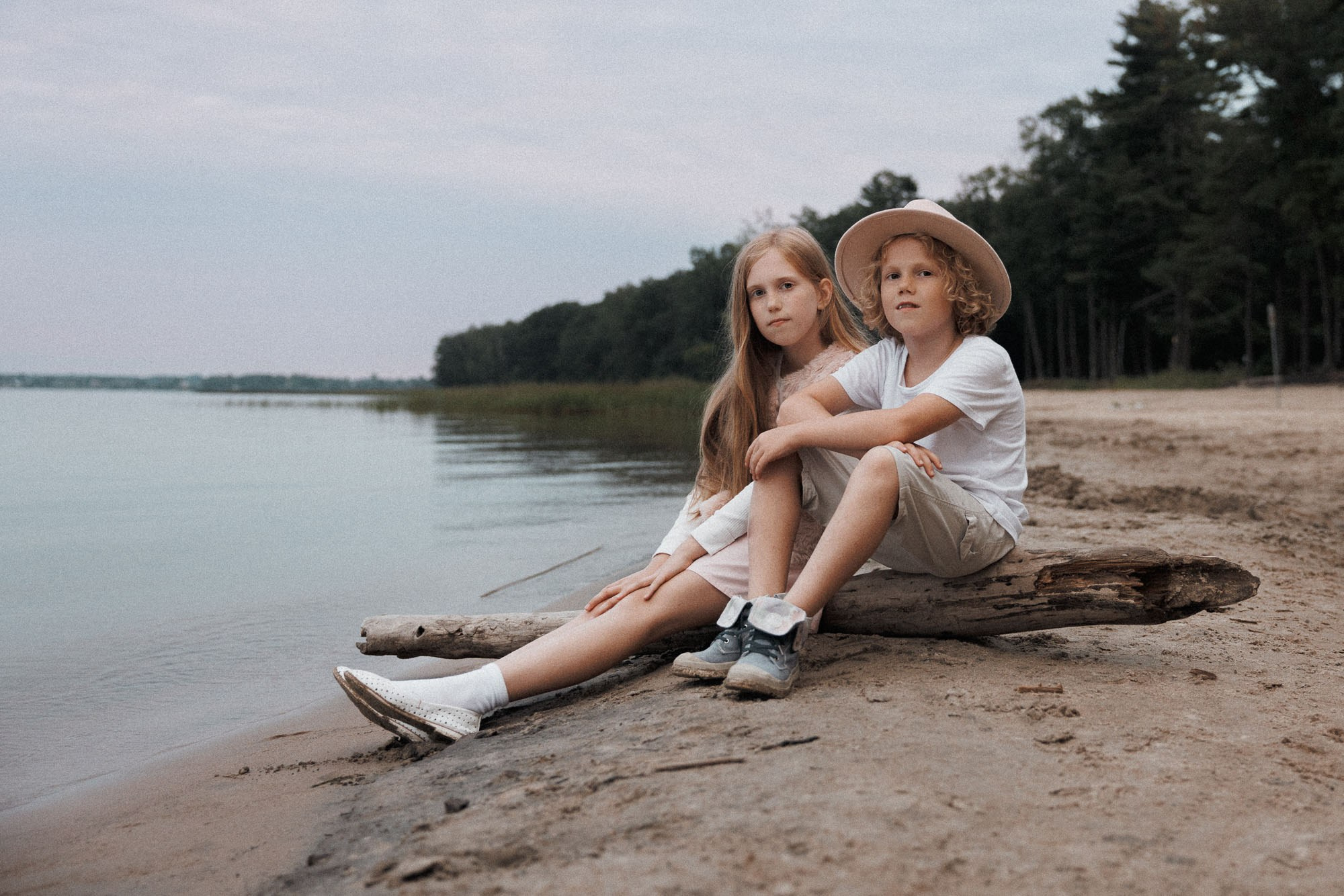Brother and sister sitting together on driftwood at the shoreline