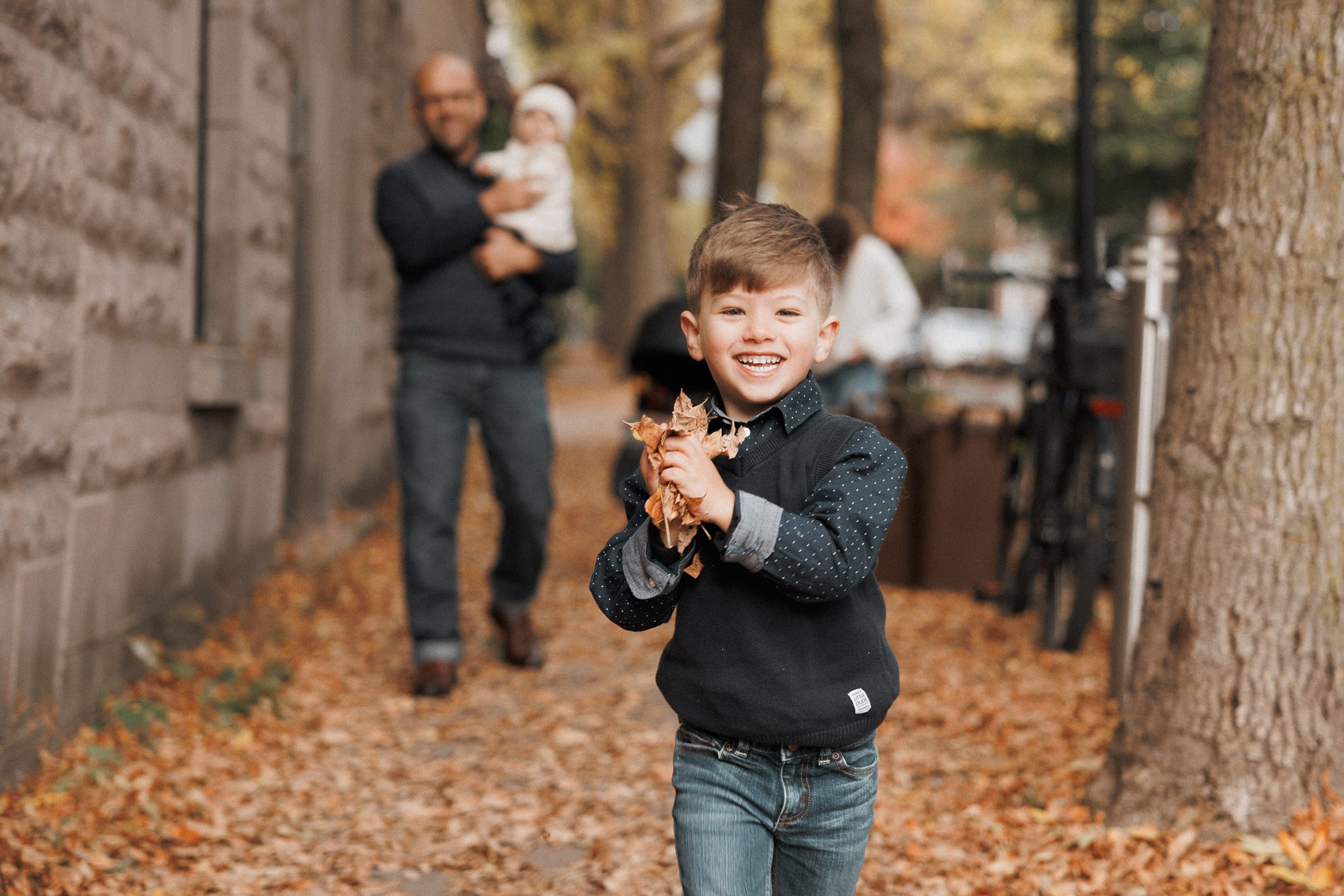 Smiling young boy holding fallen leaves during an autumn family session