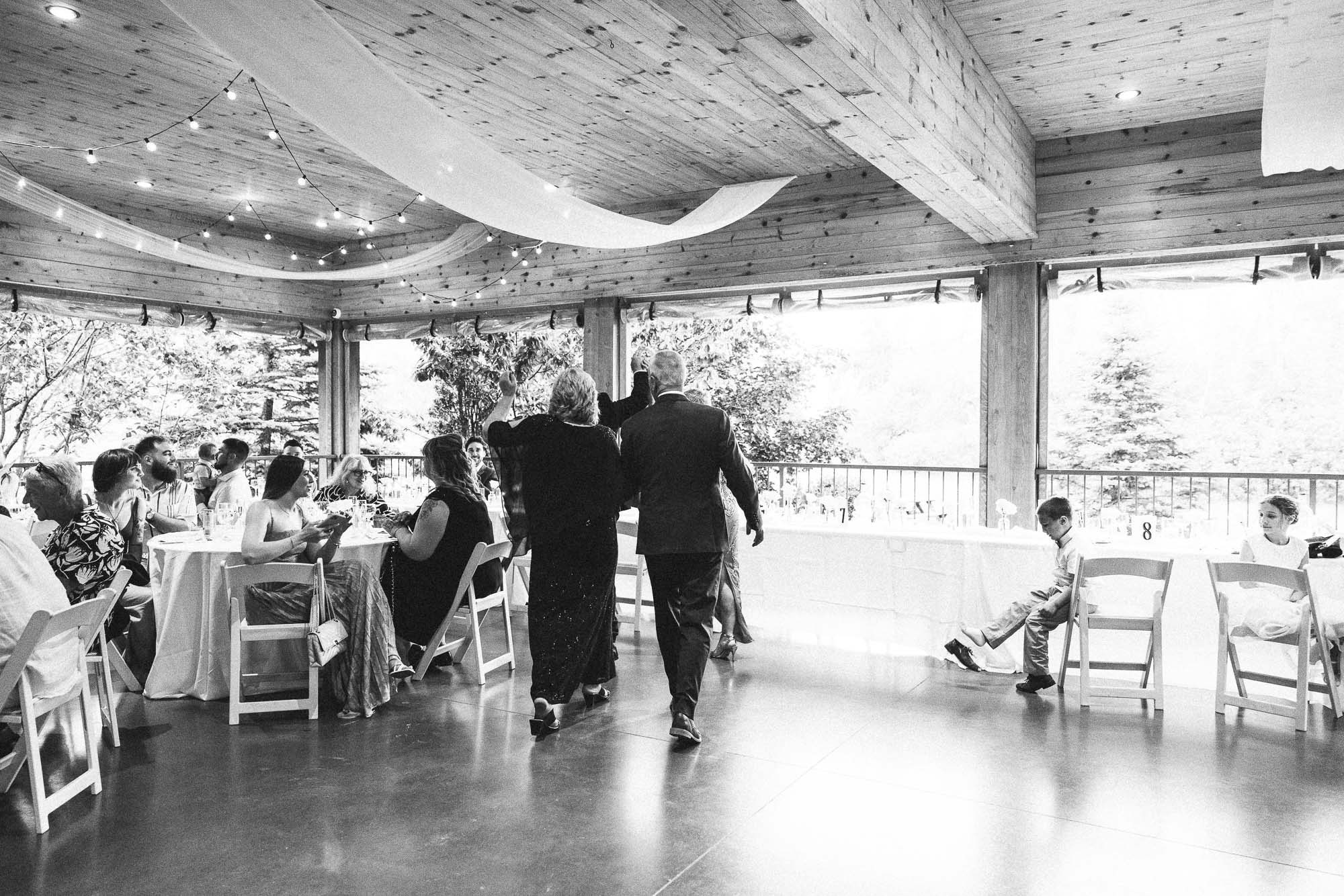 Des invités traversent la piste de danse dans une salle rustique, en noir et blanc.