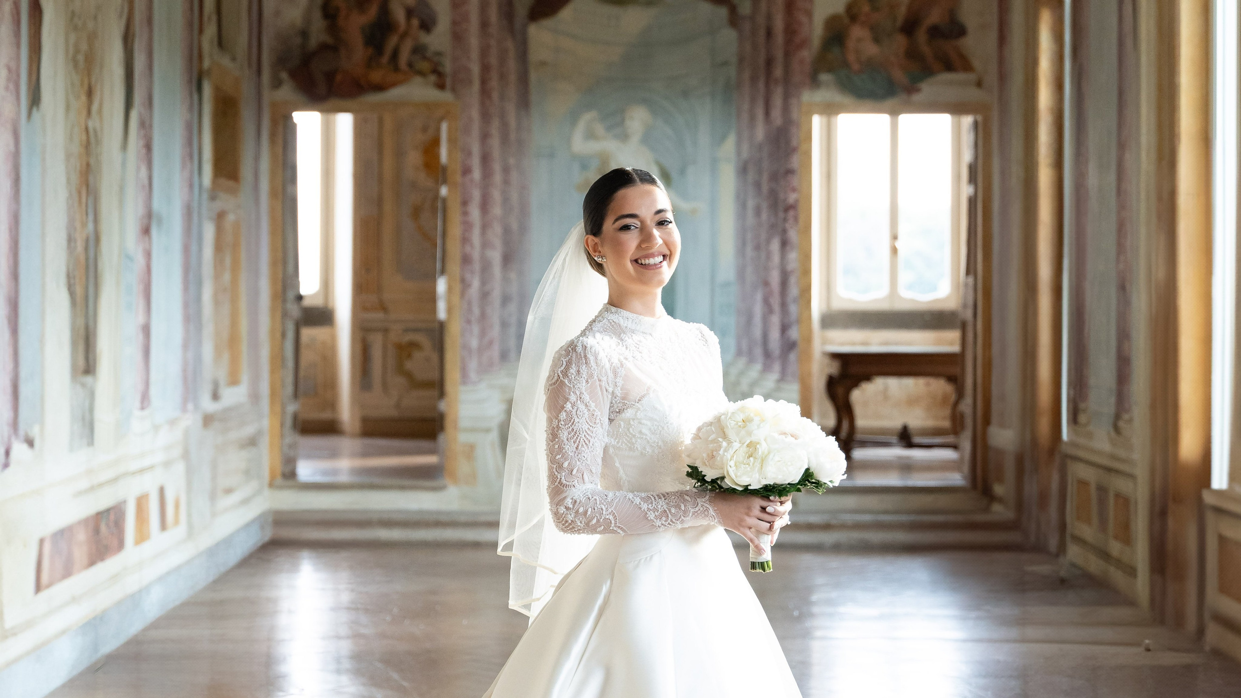 a bride in a wedding dress with a white bouquet posing smiling in villa grazioli hall
