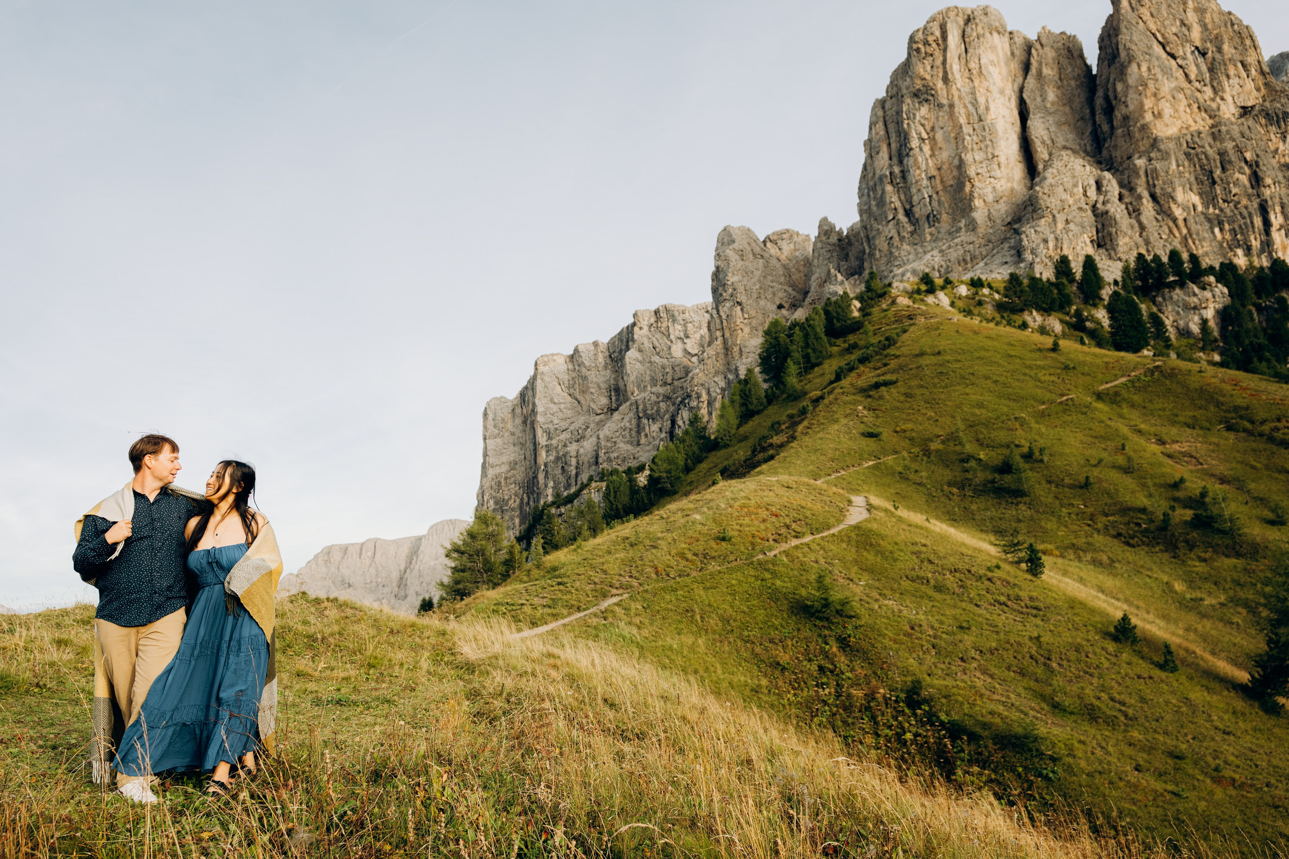 Laughing couple walking through wildflower meadow near Ortisei with mountain peaks behind – MarkartVisuals