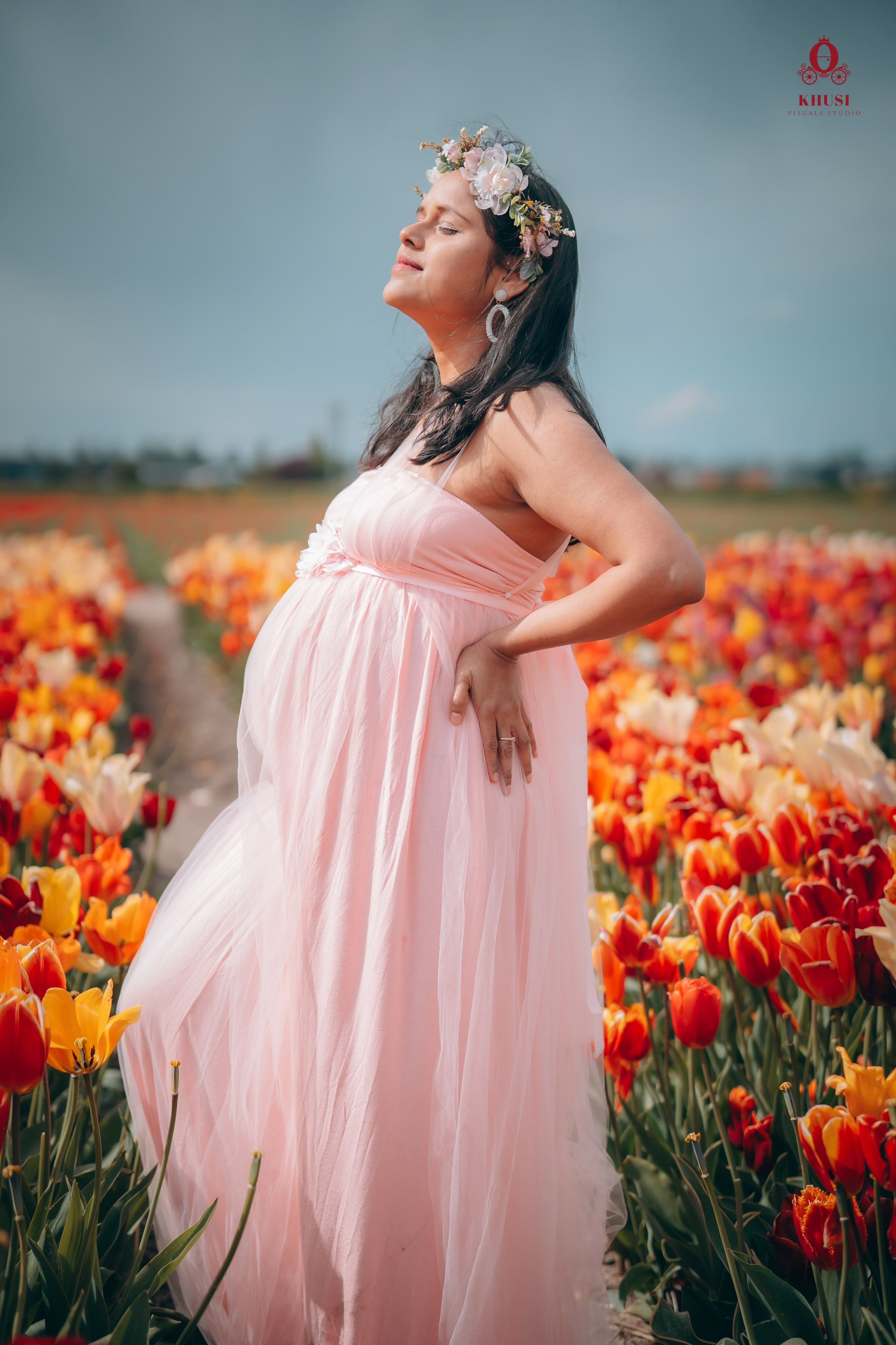 A pregnant woman standing in a tulip flower fields in netherlands and soaking up the sun