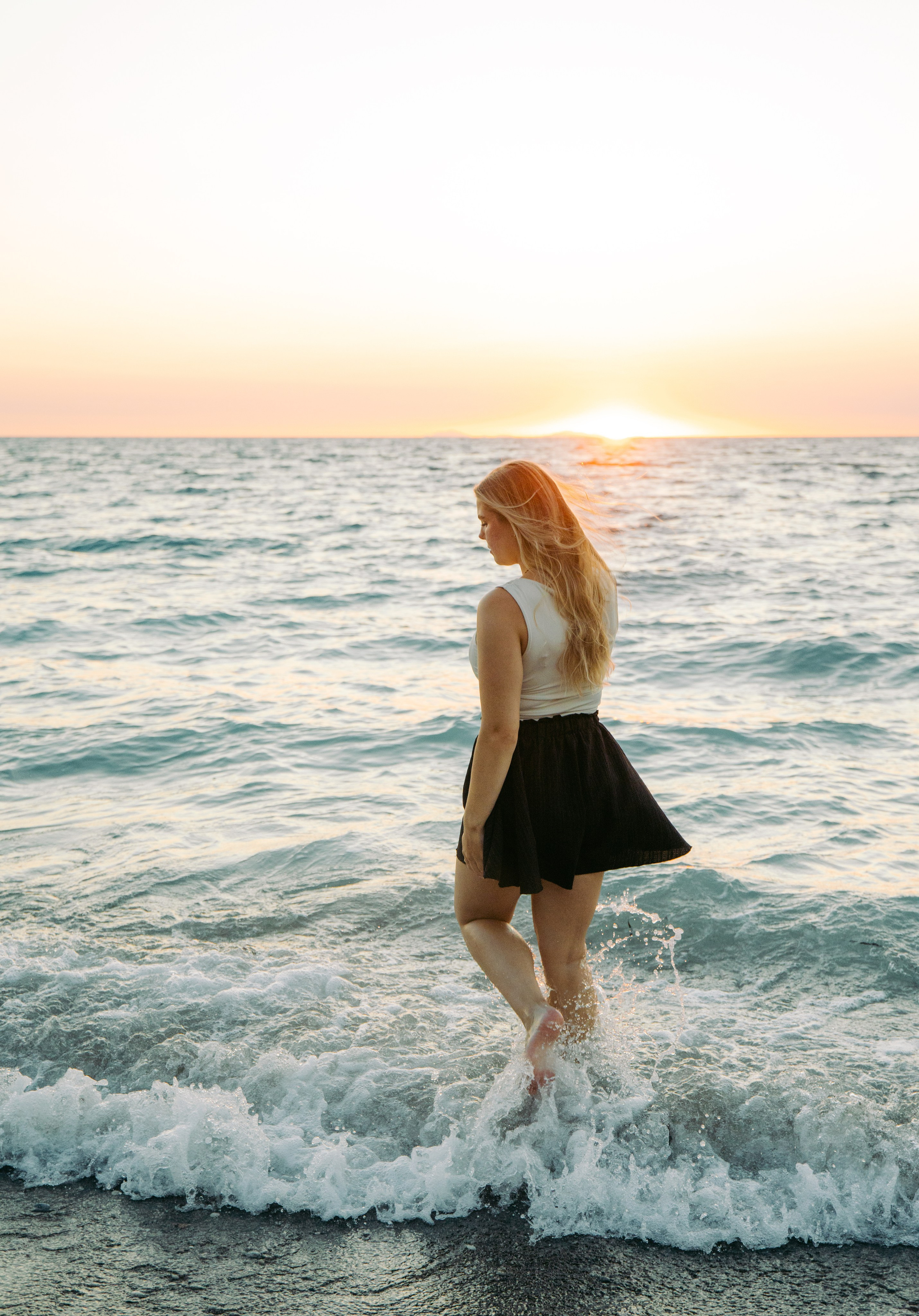 "Glücklicher Moment am Meer: Die Braut geht im seichten Wasser von Kato Petres spazieren. Das Spiel aus Schaumkronen, dunklen Kieselsteinen und dem leuchtenden Türkis des Meeres umrahmt diesen friedlichen Moment nach dem Antrag."