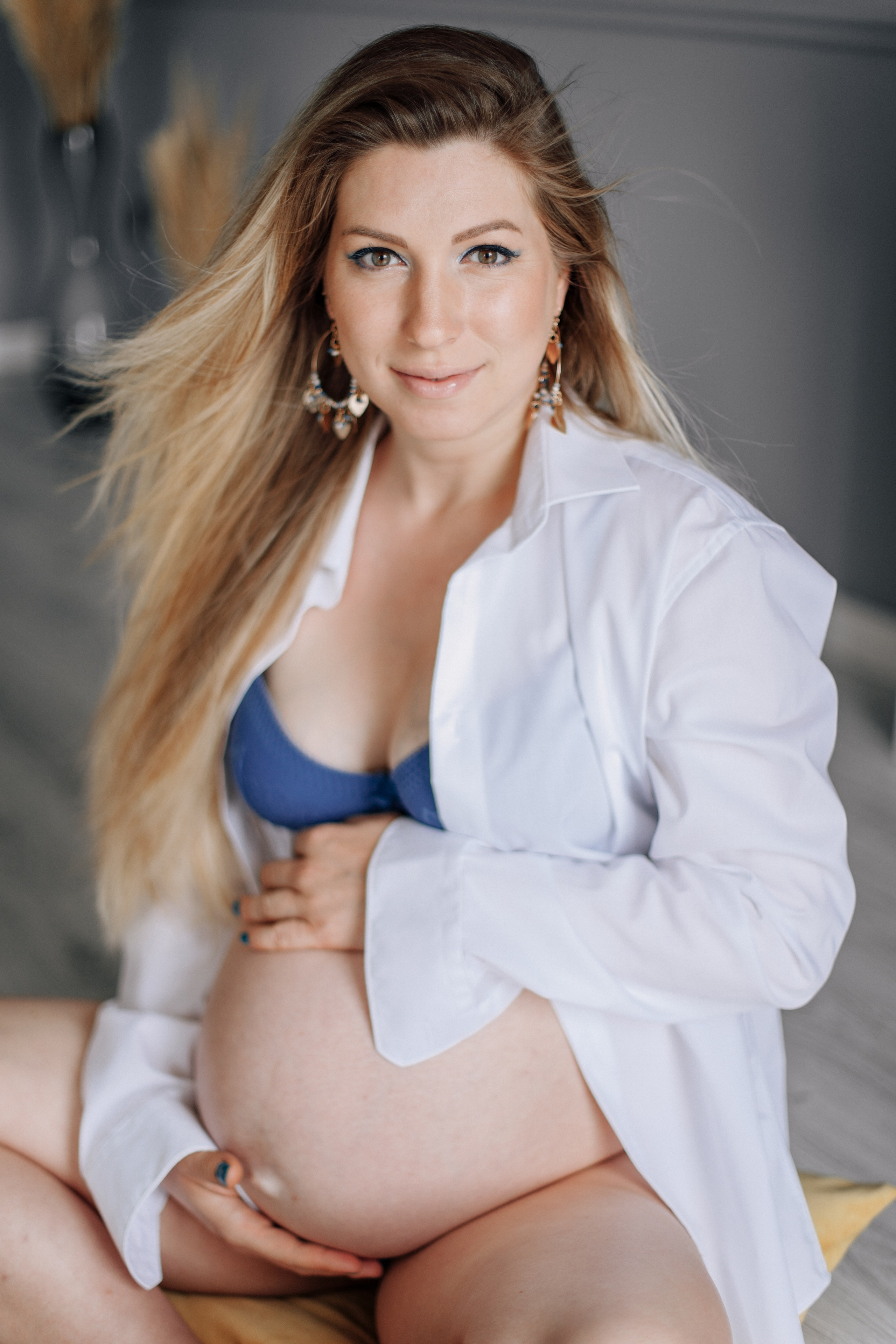 Schwangere Frau in Unterwäsche sitzt im Fotostudio und lächelt glücklich.