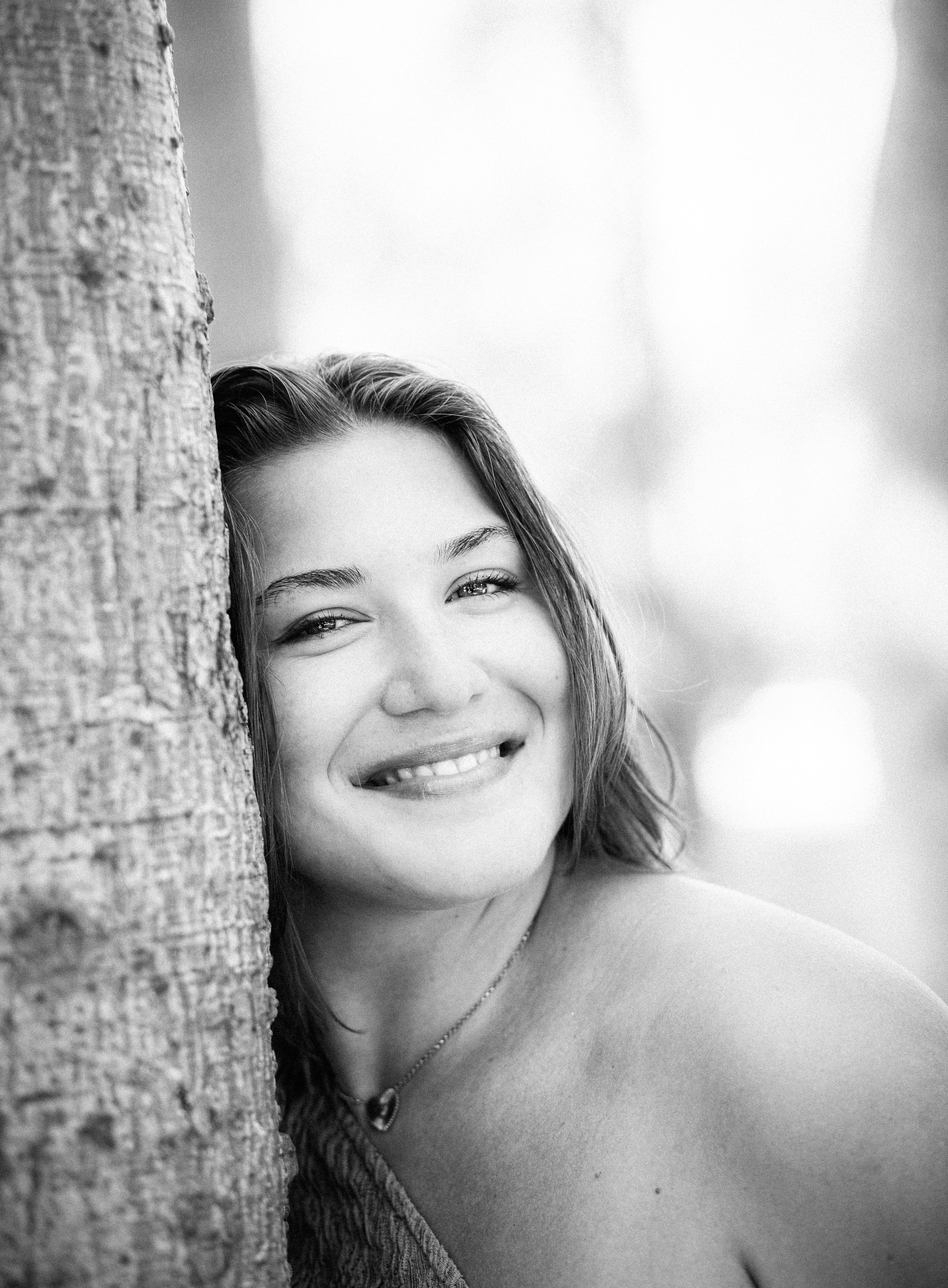Женская фотосессия в Валенсии, Испания, с естественным чёрно-белым портретом улыбающейся женщины, прислонённой к дереву, снятым в мягком свете с интимным и эмоциональным настроением — идеально для женской портретной фотографии, лайфстайл-съёмок и элегантных женских фотосессий в Валенсии и по всей Испании.