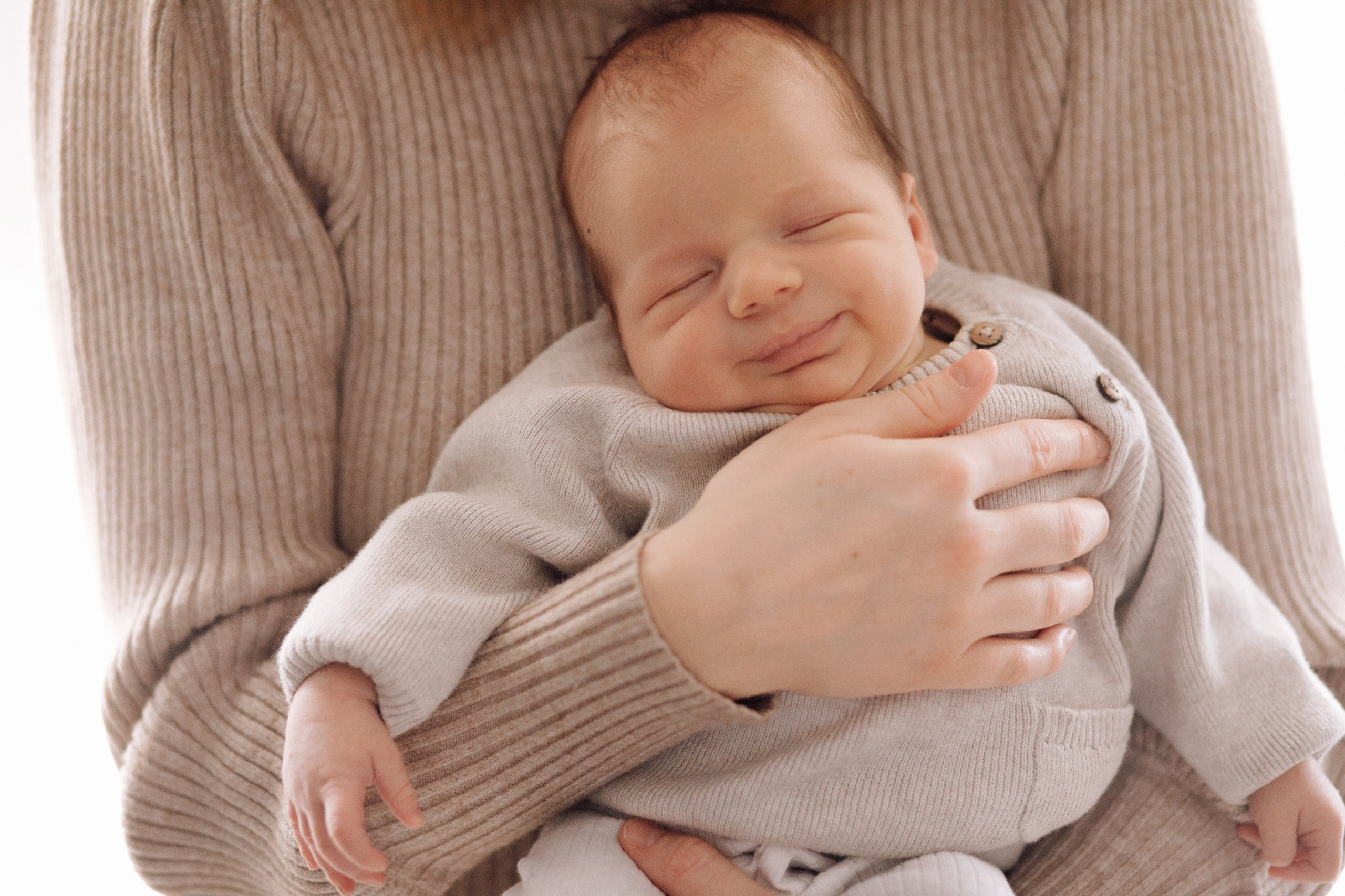 Baby lächelt in den Armen der Mutter während eines Fotoshootings. Ein glücklicher und liebevoller Moment.