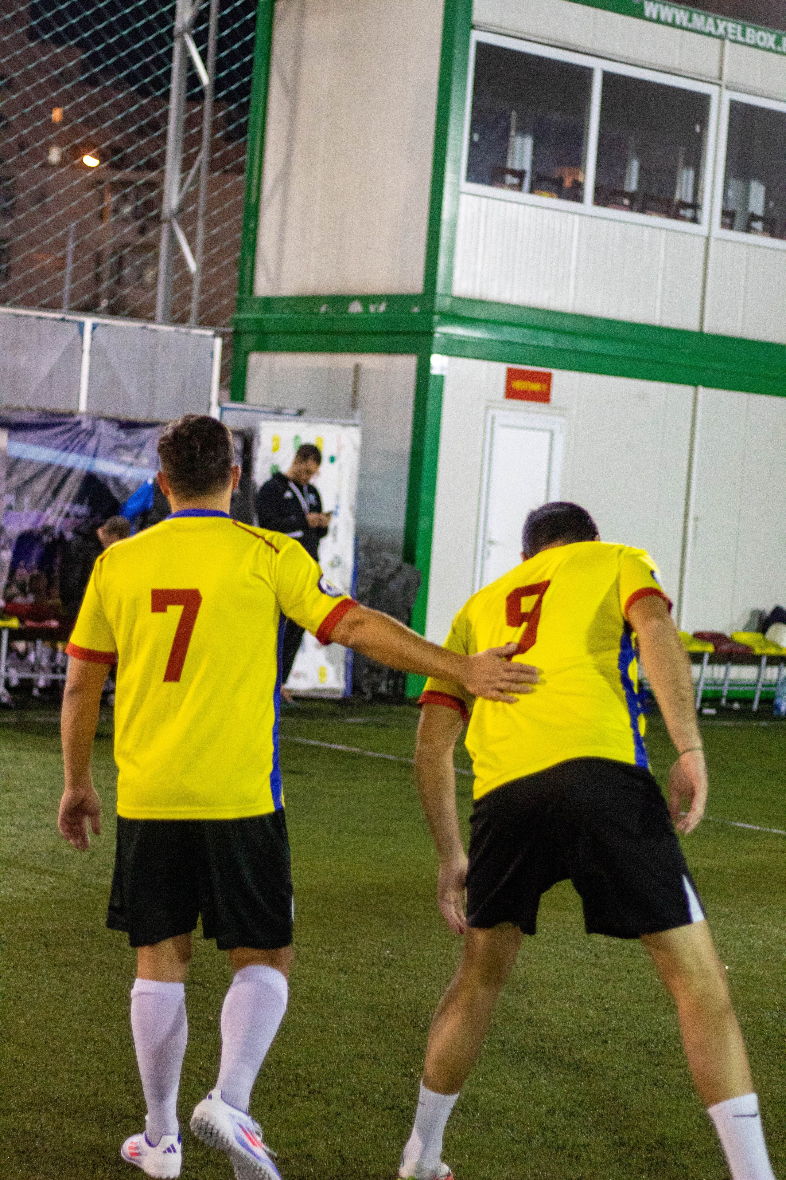 Two football players in yellow jerseys on a turf field before restarting play.