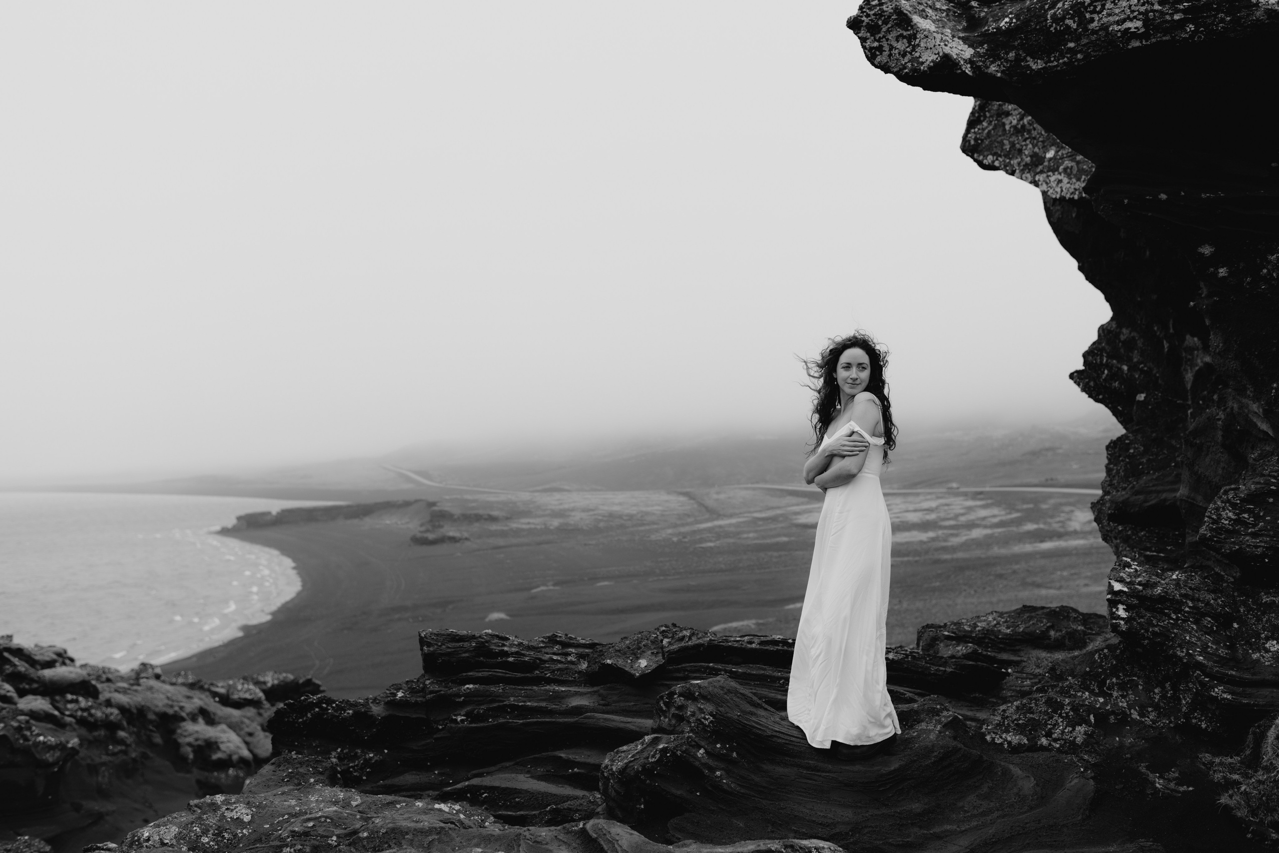 Bride in a flowing dress and groom in a traditional Icelandic sweater, walking across the rocky terrain of Krýsuvík.