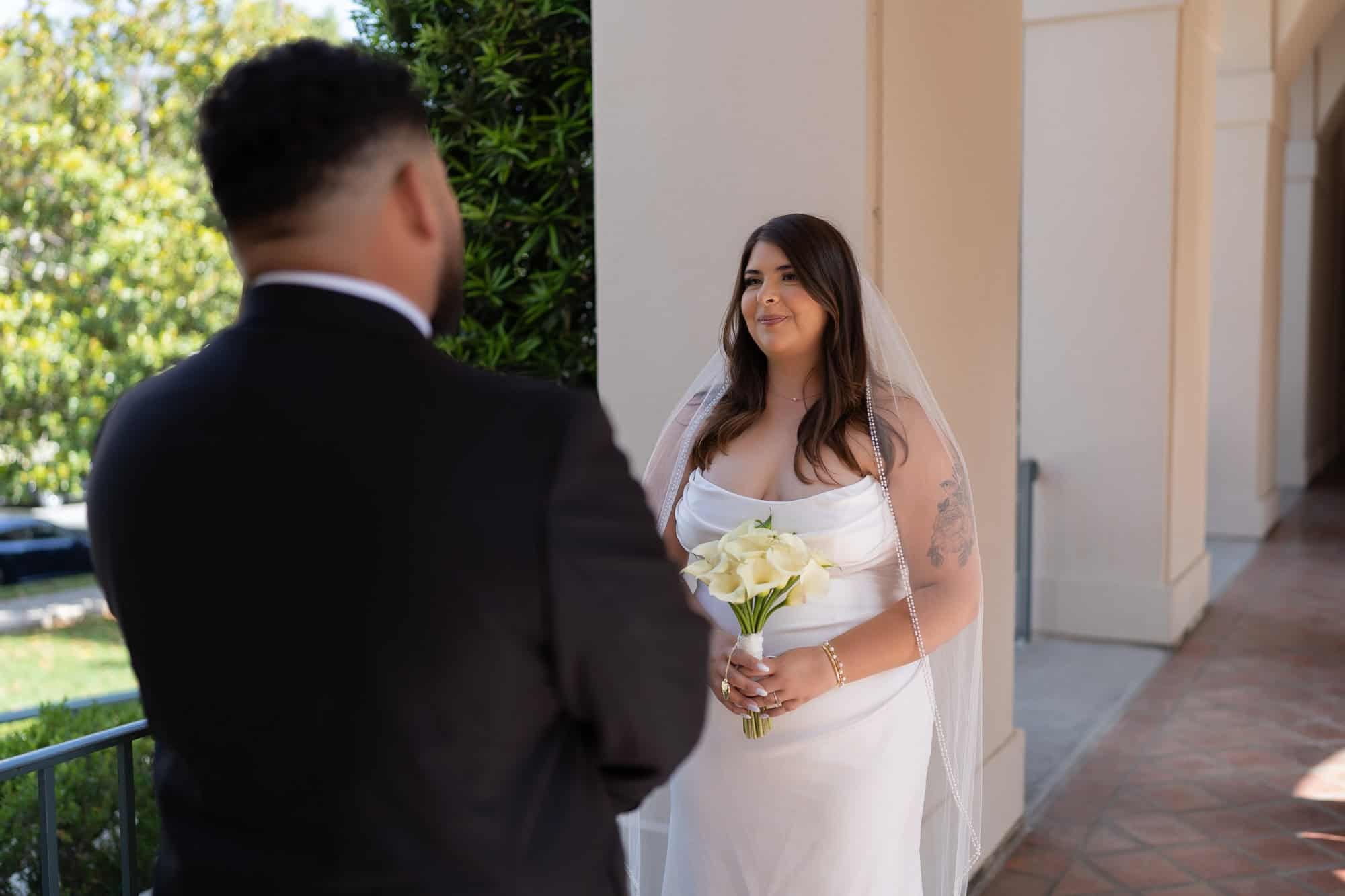 Groom smiling at bride holding bouquet in the courtyard