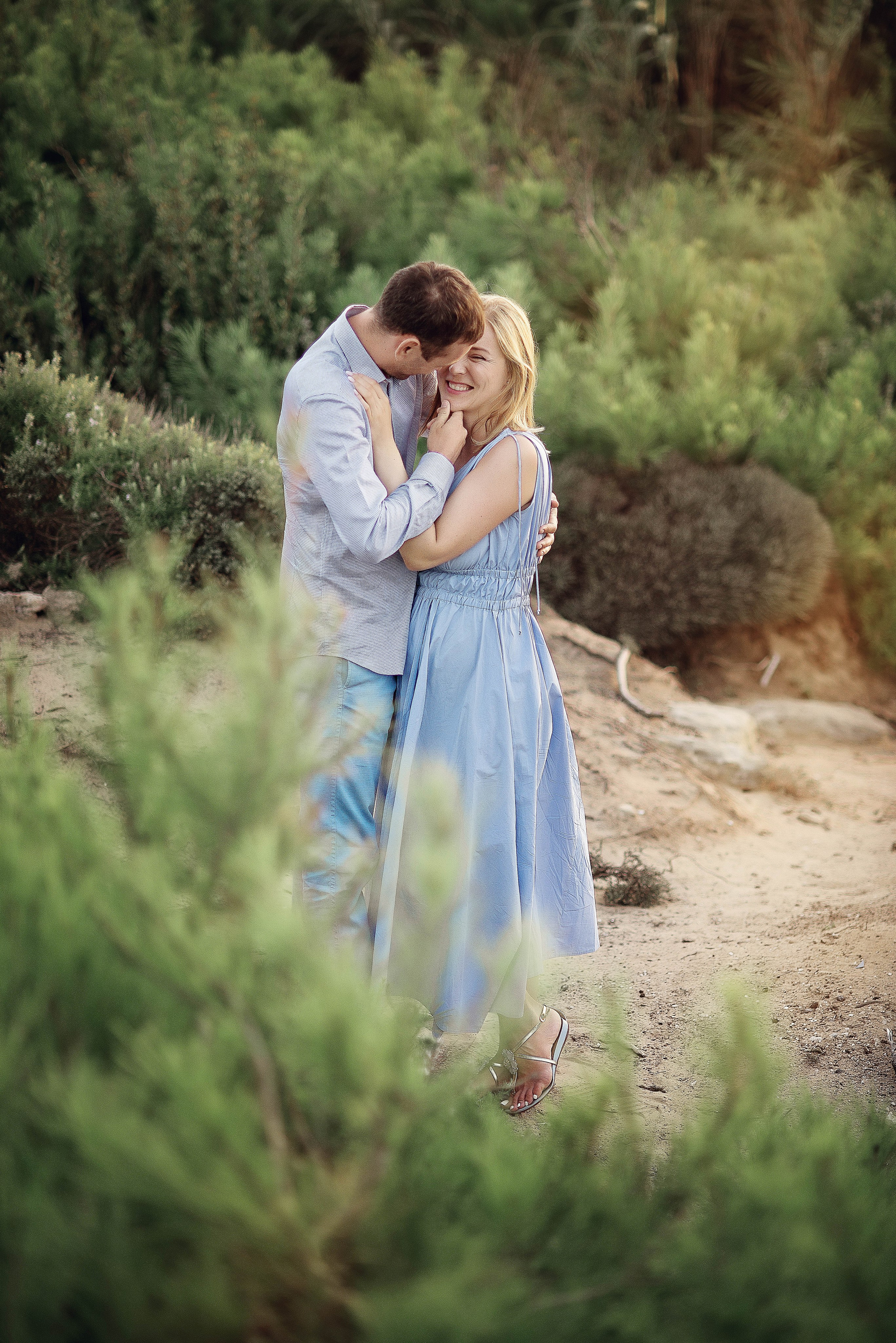 Surrounded by Mediterranean vegetation, the couple shares a tender embrace on a coastal trail.