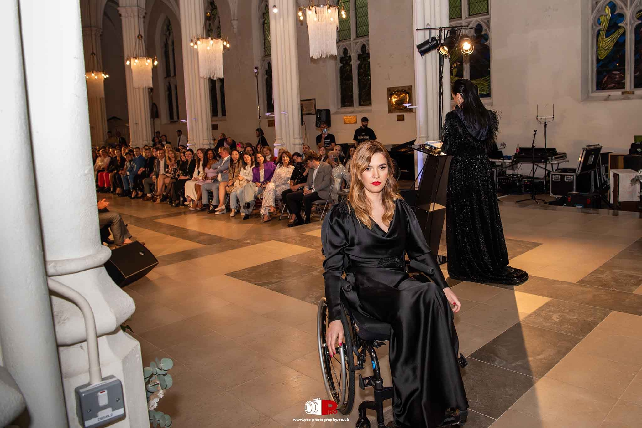 A model in a sleek black dress in a wheelchair making a powerful runway appearance at the MAD-Aid Gala.
