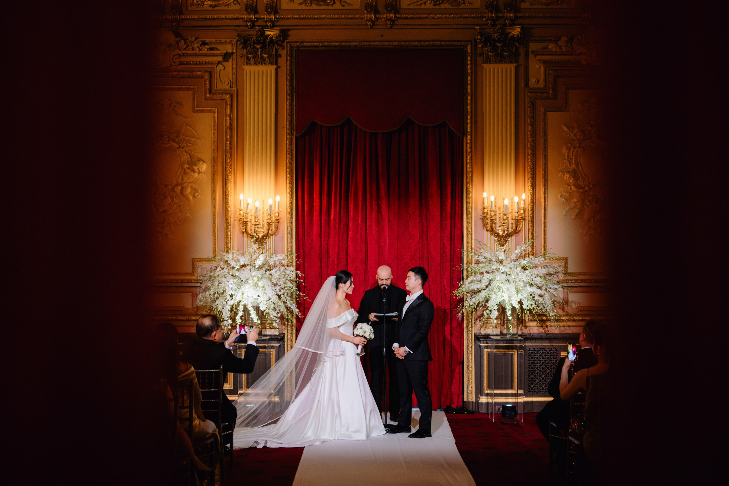 a bride and groom standing in front of a red curtain