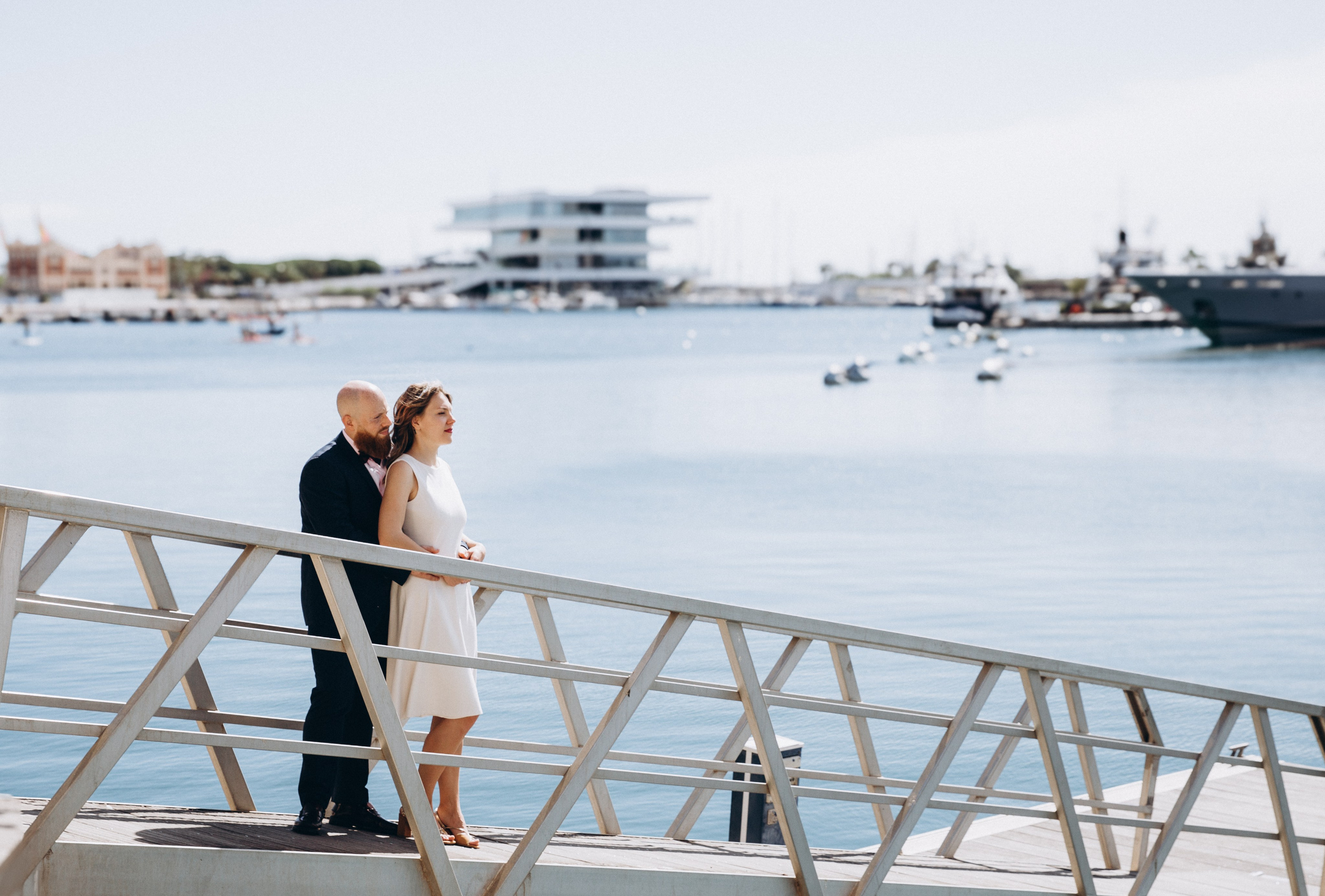 Romantic waterfront wedding photoshoot in Valencia, Spain — elegant couple embracing on a modern marina bridge with the iconic Veles e Vents building in the background, capturing love, intimacy, and architectural charm. Perfect for couples searching for stylish and memorable wedding photography in Valencia and coastal Spain.
