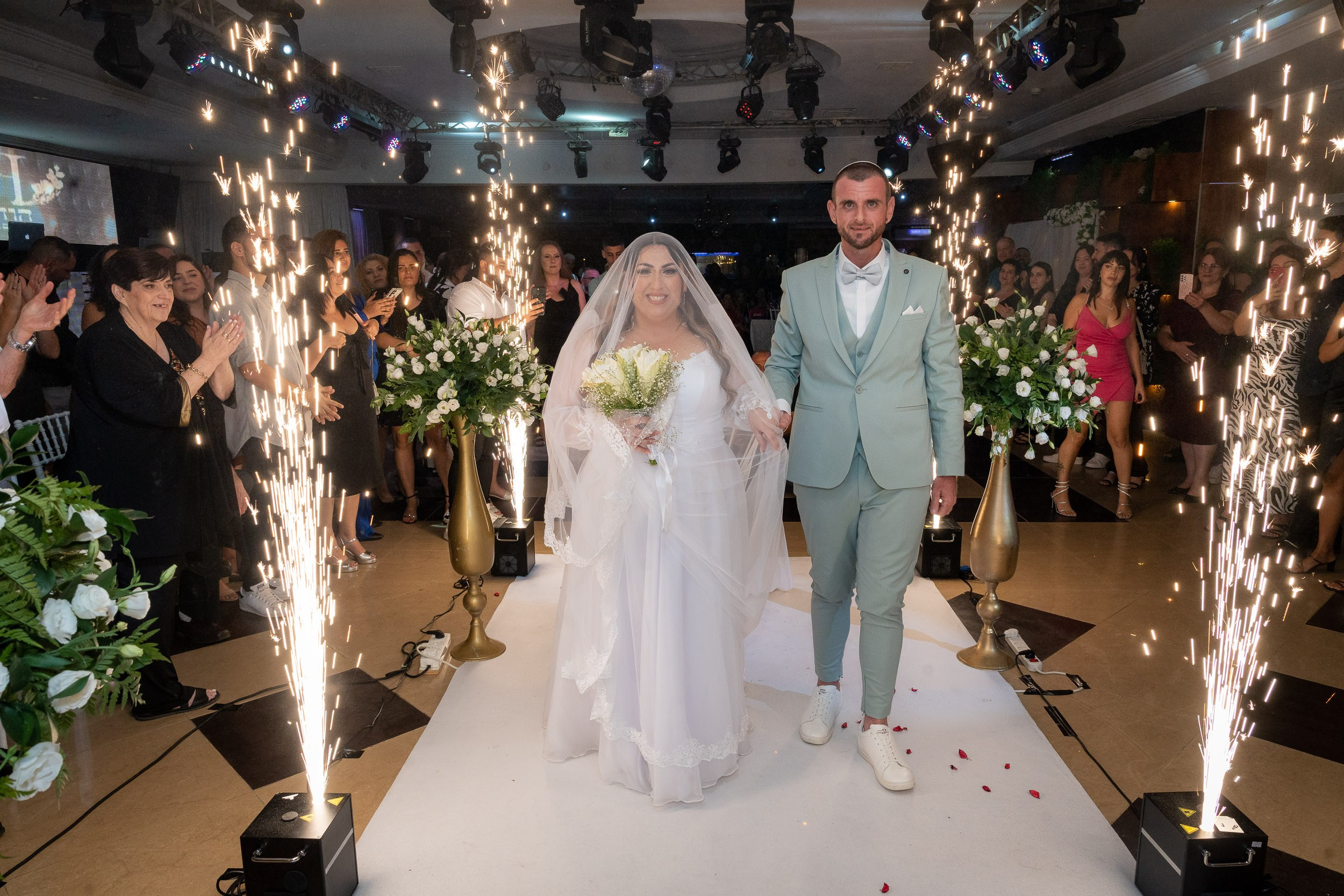 Ella and Matan walk down the aisle surrounded by cold sparklers