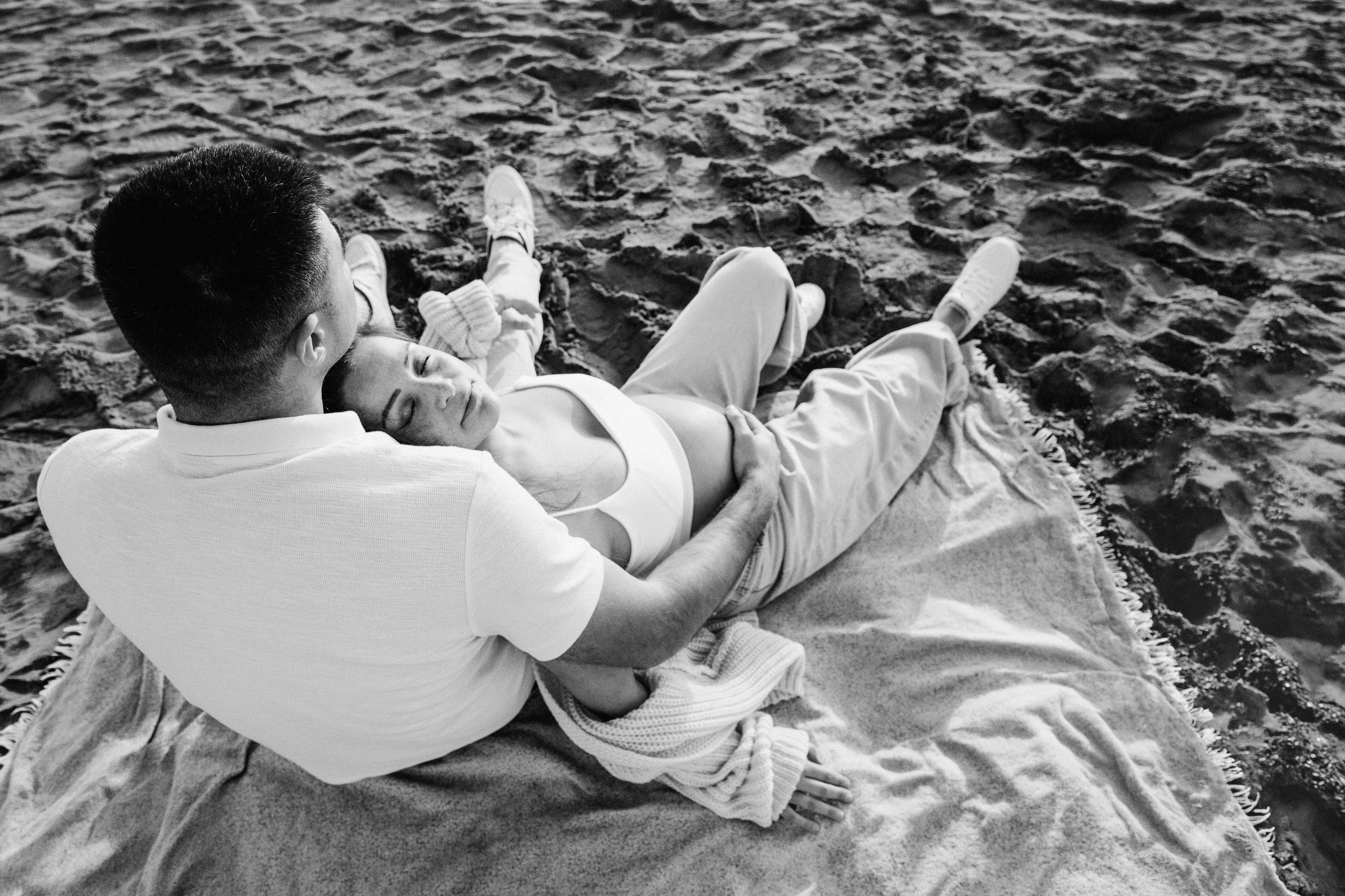 Sesión de fotos de embarazo en Valencia, España, con una pareja tumbada junta al aire libre en un momento relajado e íntimo, capturada en blanco y negro para una escena lifestyle atemporal — ideal para sesiones maternity en Valencia y España.