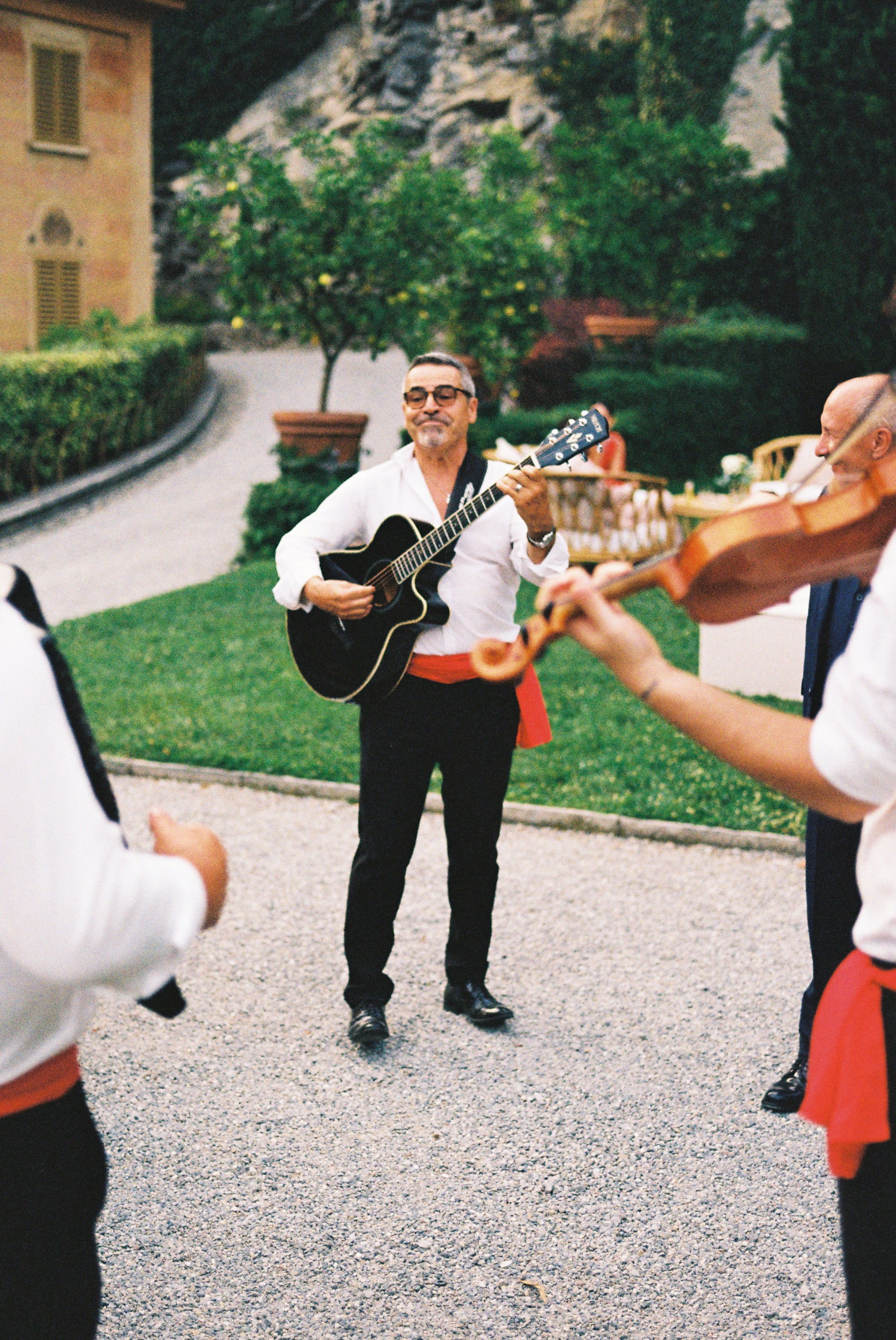 Guitarist smiles while playing for guests at an outdoor wedding celebration.