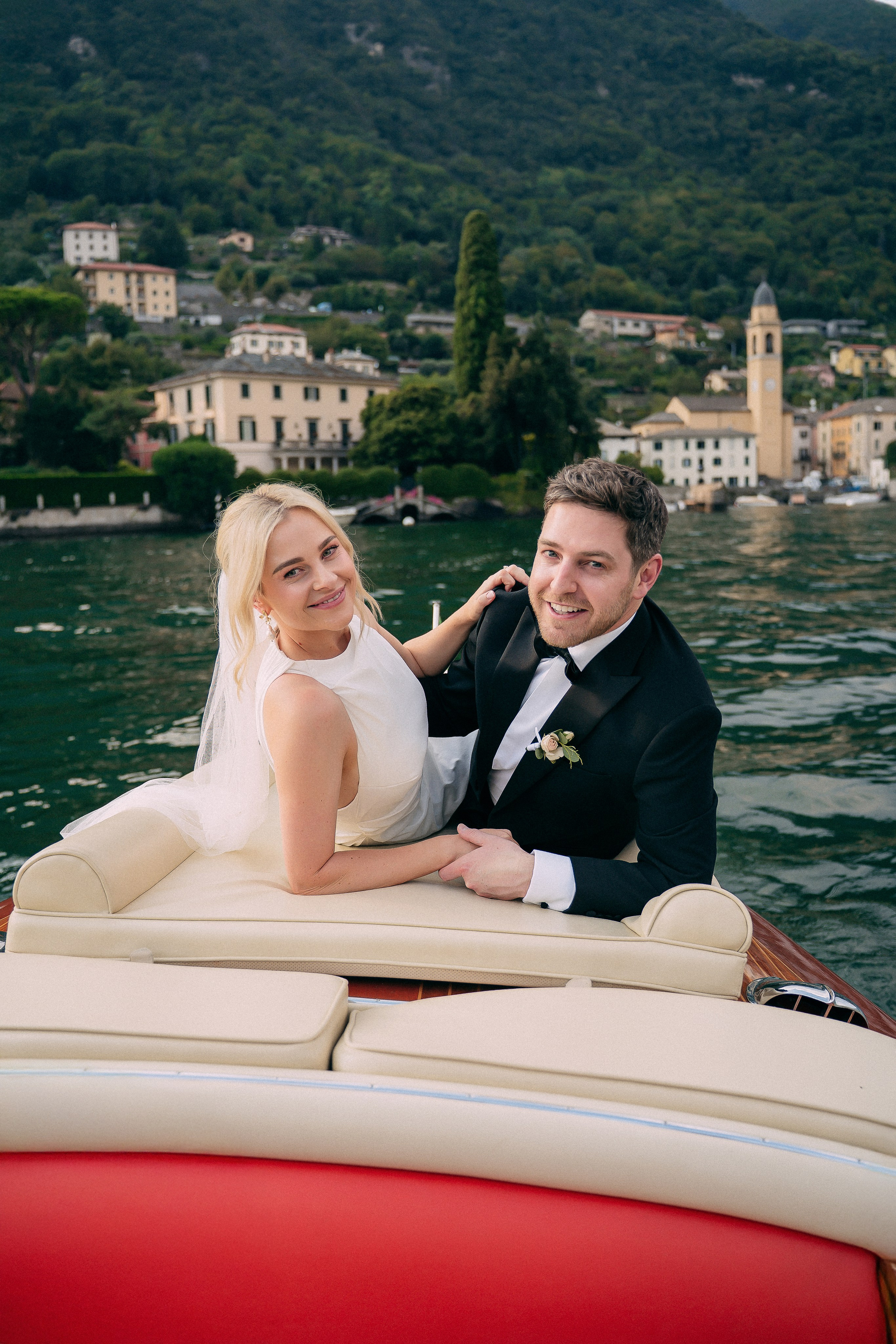 Bride and groom sitting on the boat with the village view at Villa Lario, Lake Como, Italy