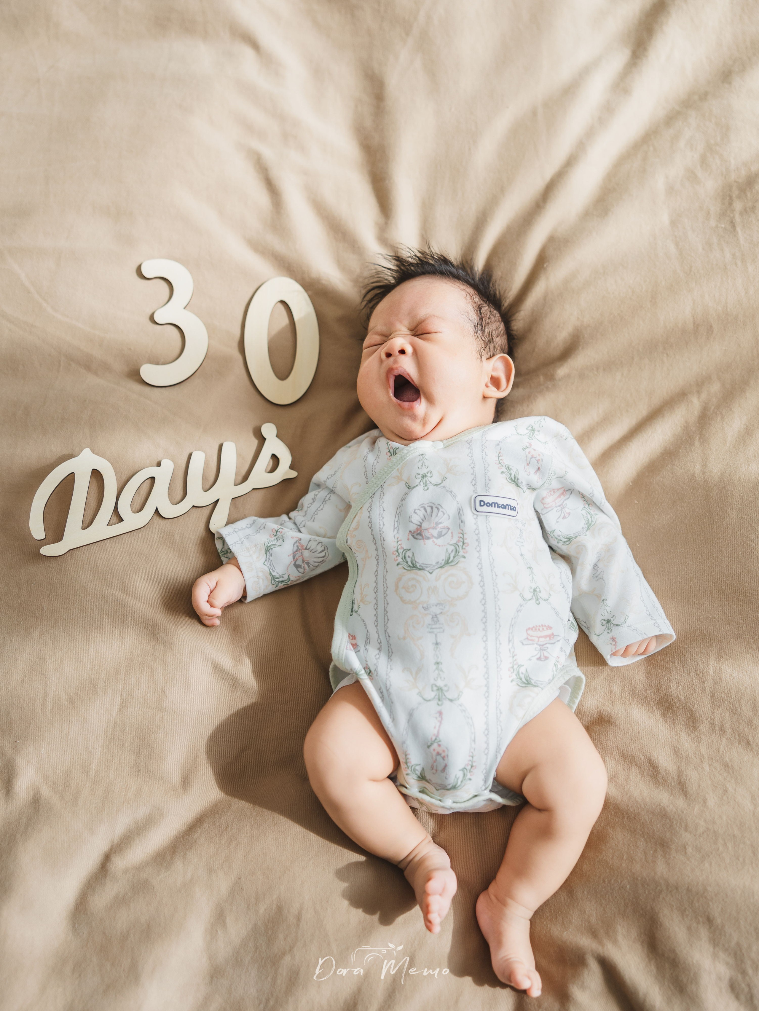 One-month-old baby lying on the bed with “30 days” sign, milestone baby photography in natural light in Shanghai.