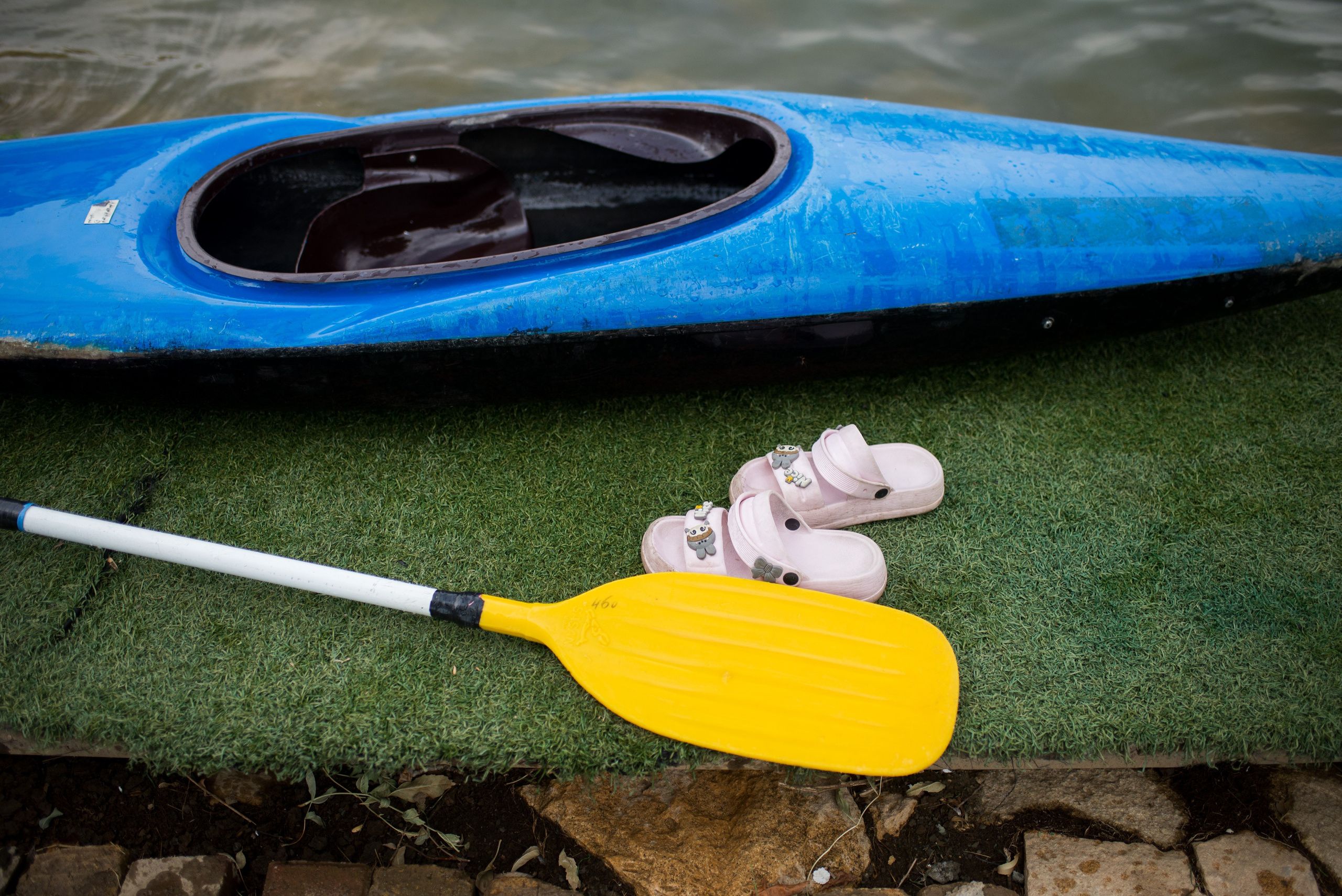A young team member’s sandals lie beside a kayak and a paddle at the training site.