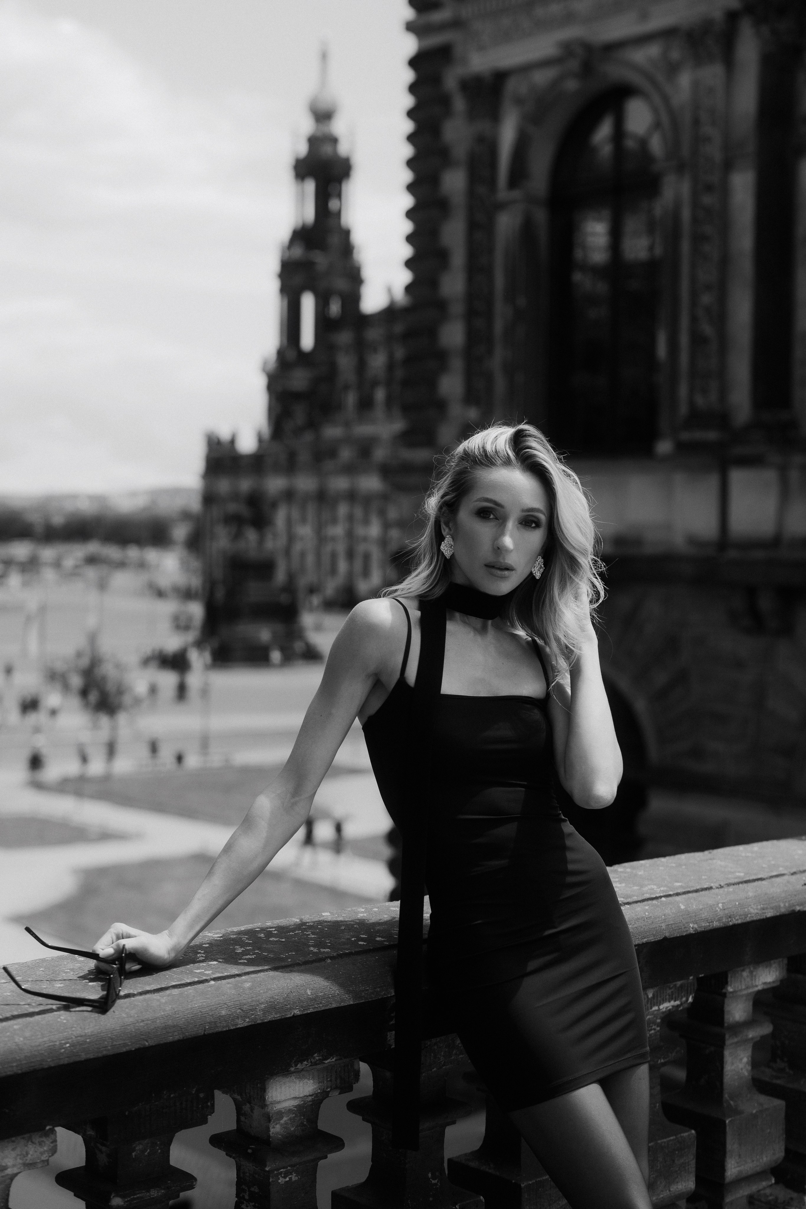 Black and white portrait of an elegant blonde woman in a black dress standing on a historic terrace in Dresden, Germany. Timeless female portrait photography by a black and white photographer serving Dresden, Leipzig and Wurzen. Чёрно-белый портрет элегантной блондинки в чёрном платье на исторической террасе в Дрездене, Германия. Вневременная женская портретная фотография от фотографа, работающего в Дрездене, Лейпциге и Вурцене.