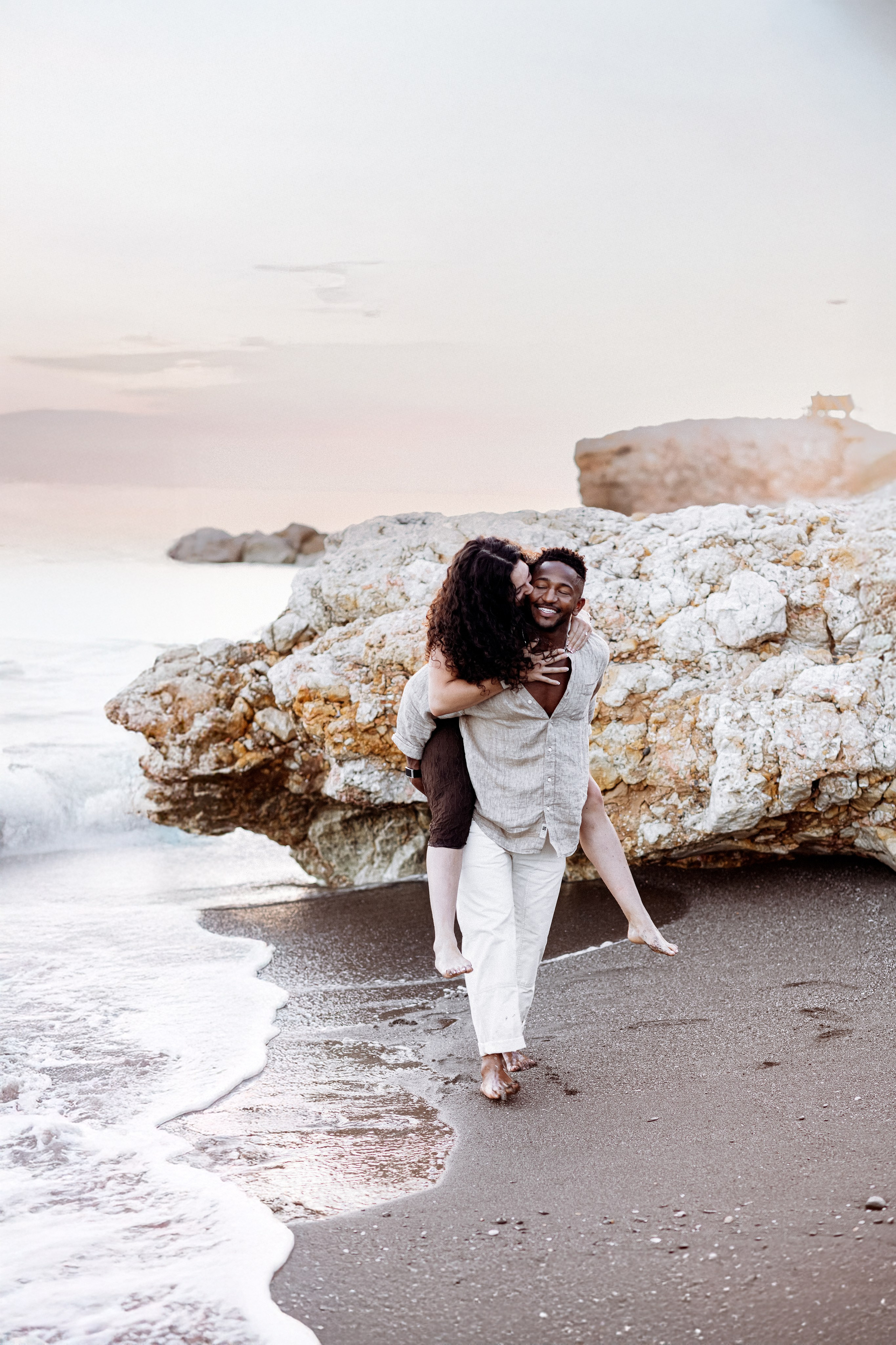 Sesión alegre y romántica en la playa de Valencia, España, capturando un momento divertido a caballito junto al mar — ideal para parejas que buscan una sesión natural y llena de amor en Valencia y en toda España.