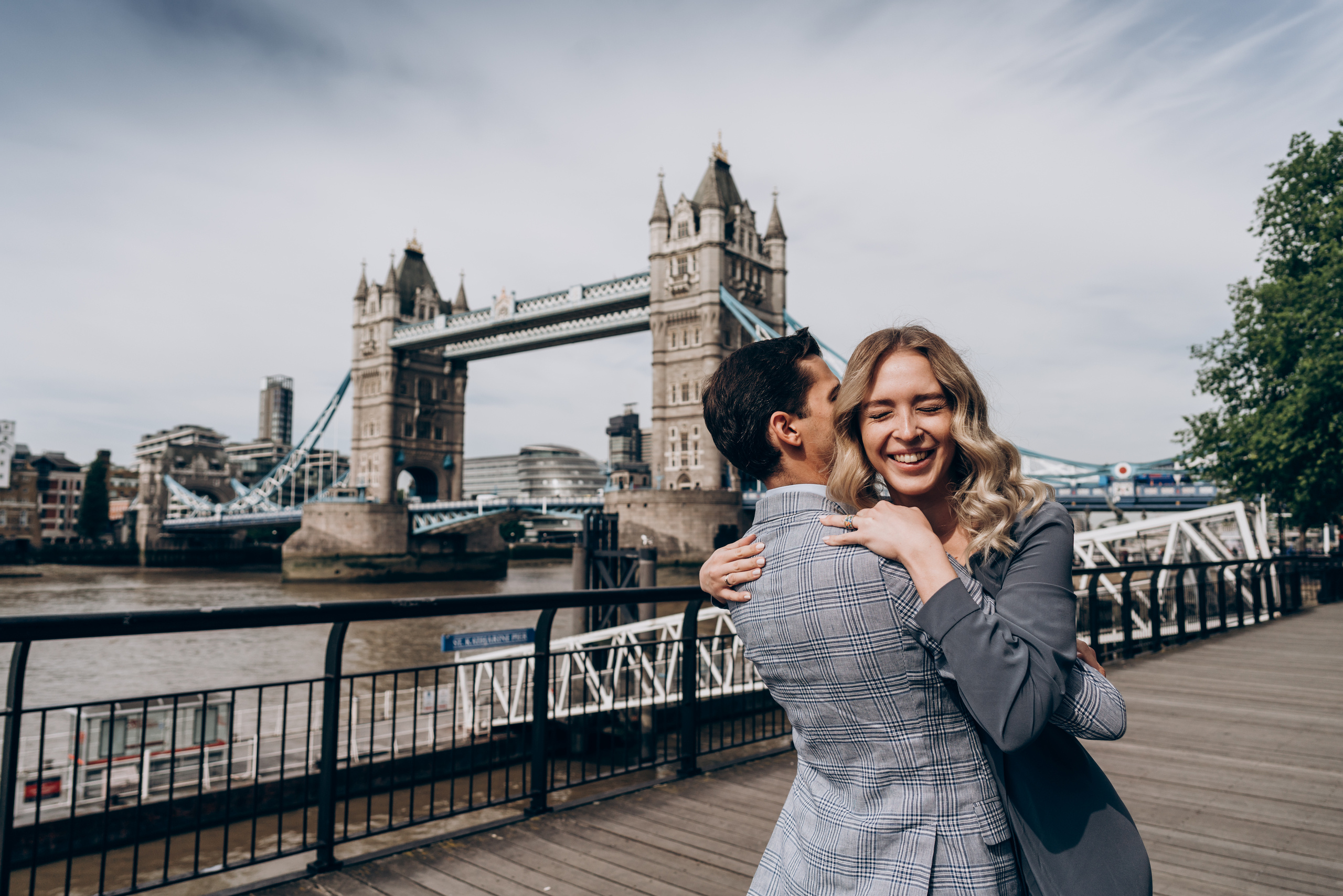 young women is hugging her fiancé by tower bridge 