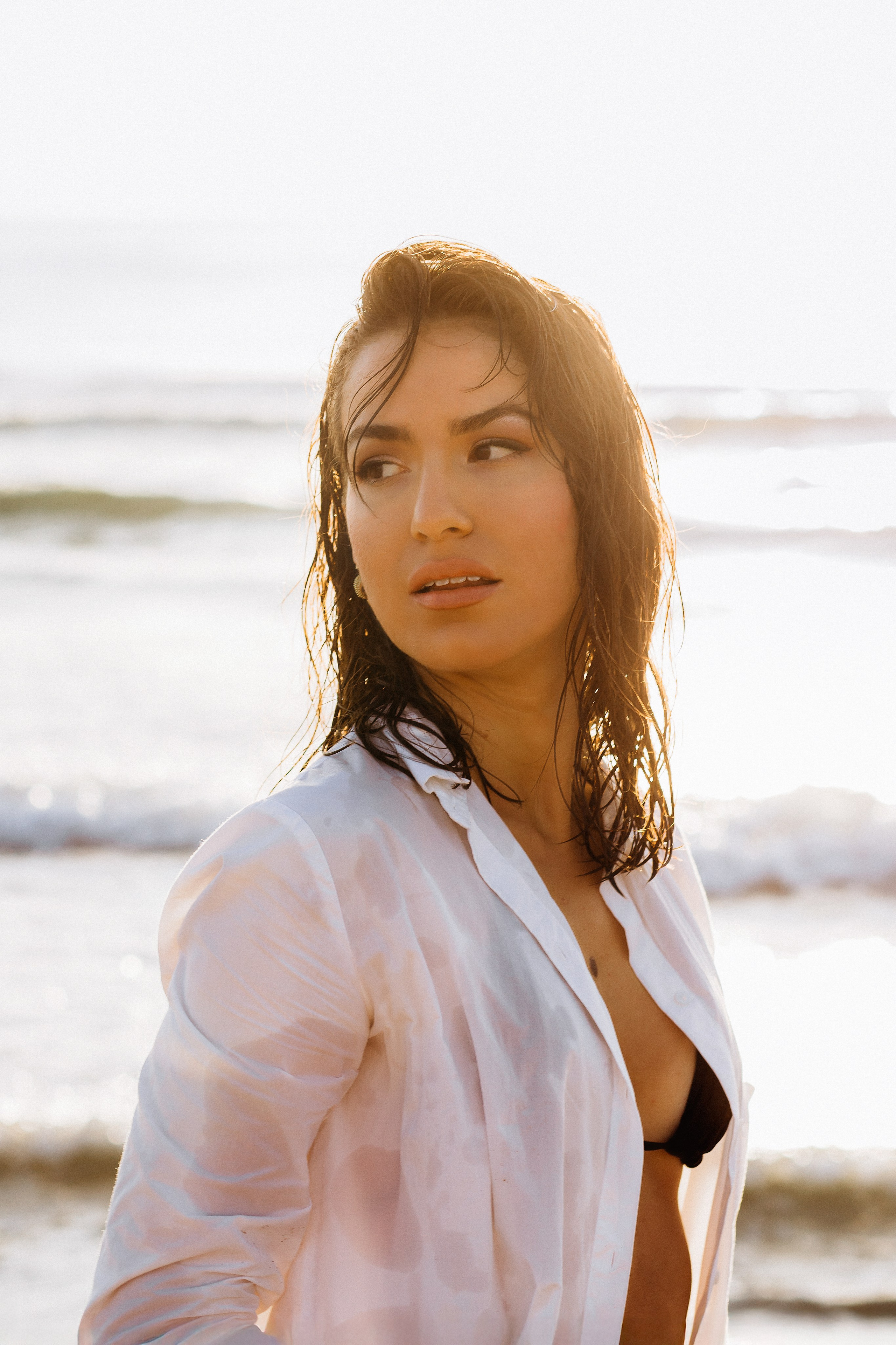 Портрет на пляже в золотой час в Сан-Себастьяне, Испания — женщина с мокрыми волосами и в расстёгнутой белой рубашке. Пример естественной и эмоциональной пляжной портретной съёмки в Сан-Себастьяне и прибрежных районах Испании.