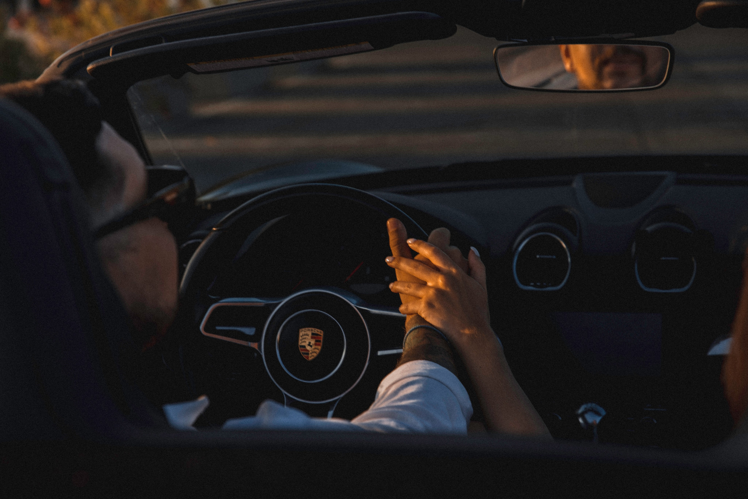 Sesión de fotos love story de pareja en València, España, capturando un momento íntimo de una pareja cogida de la mano dentro de un lujoso coche descapotable durante la golden hour, con la cálida luz del atardecer mediterráneo reflejándose en el parabrisas y creando una atmósfera romántica y cinematográfica — ideal para fotografía de pareja, sesiones love story, reportajes de compromiso, retratos lifestyle de pareja y sesiones románticas en València y en toda España.