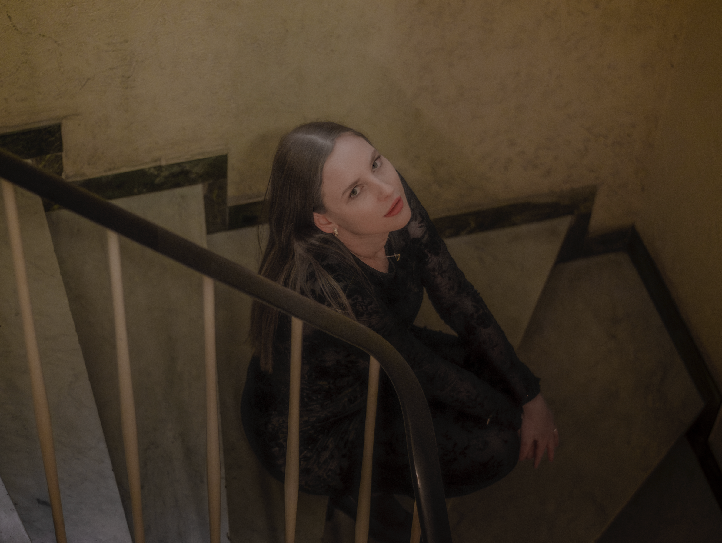 Porträt einer jungen Frau mit dunkelblonden Haaren und schwarzem Spitzenkleid sitzend im Treppenhaus