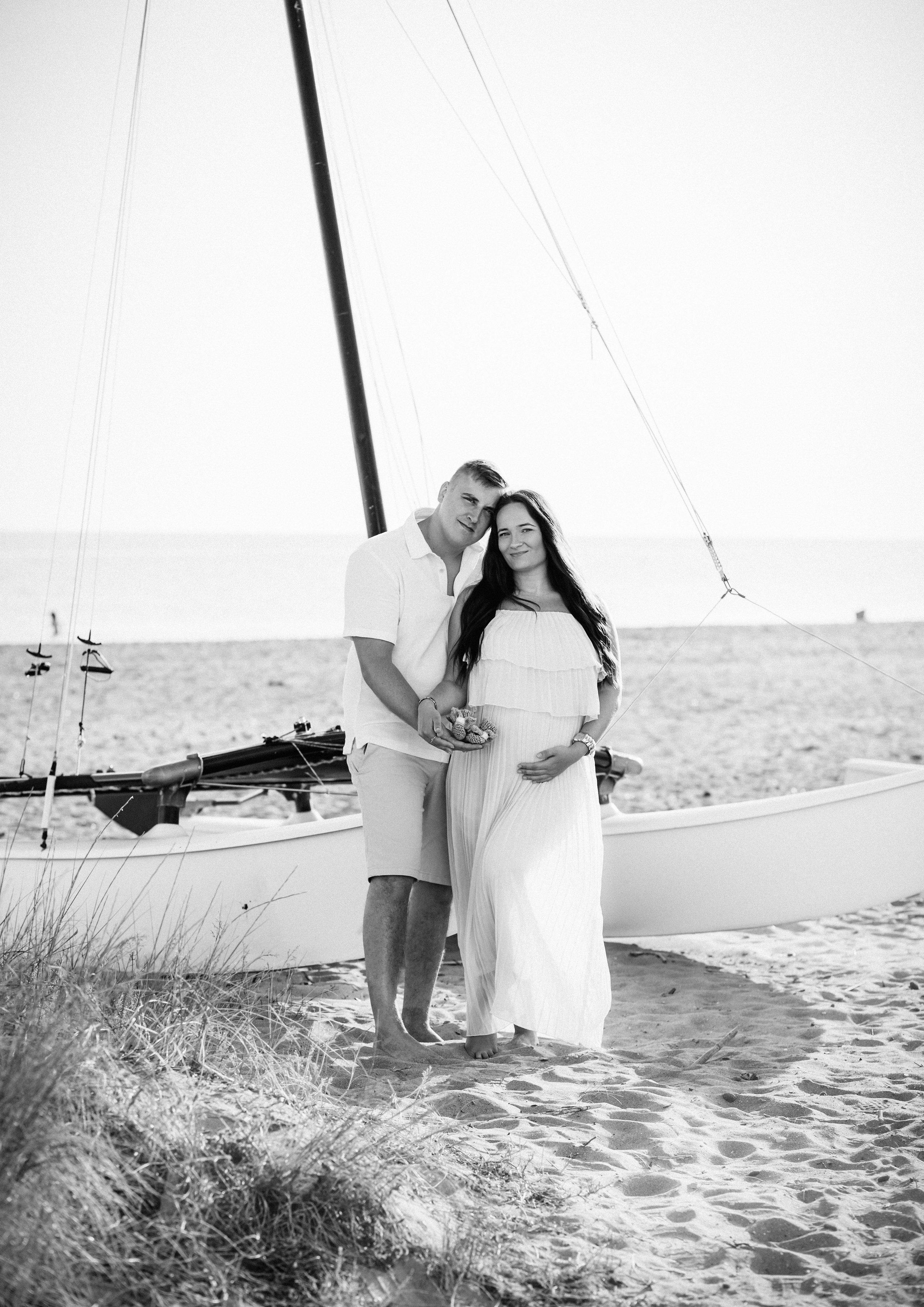Sesión romántica de embarazo en la playa de Benidorm, España — pareja abrazada junto a un velero, capturando ternura y calma marina.