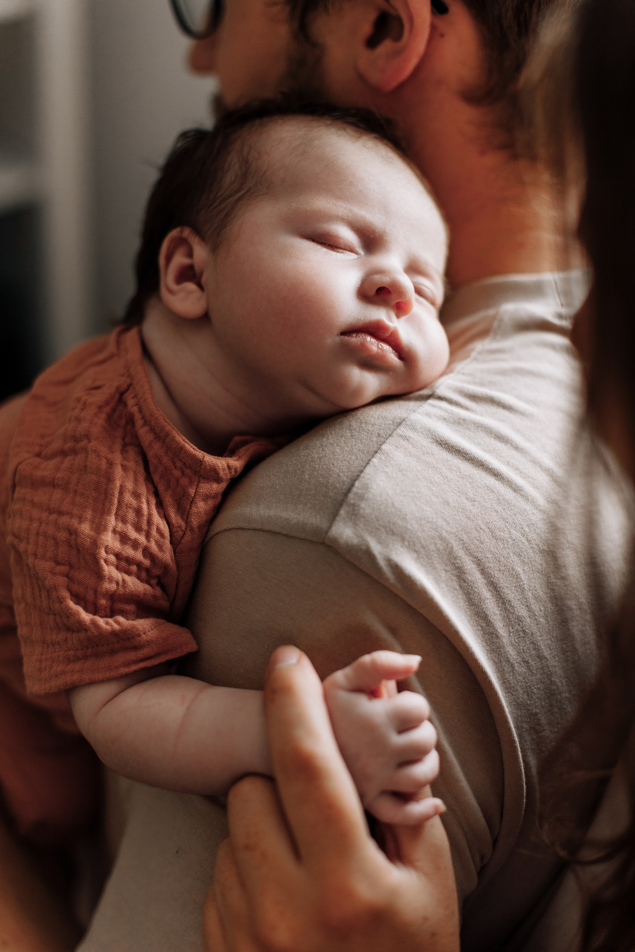 Mädchen schläft auf der Schulter des Vaters, während die Mutter ihre Hand hält. Ein liebevoller und friedlicher Familienmoment.