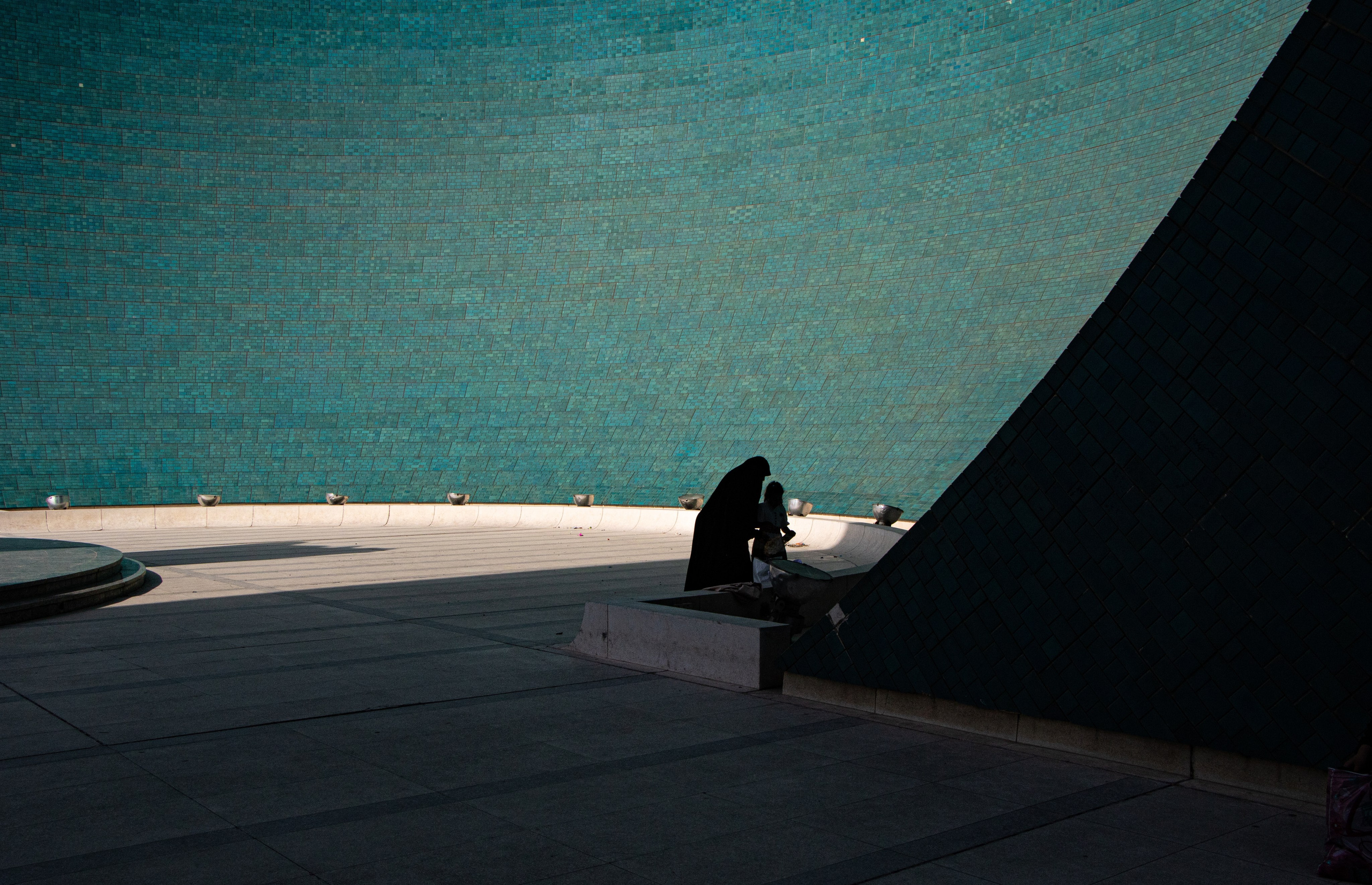 Une femme irakienne et son enfant se tiennent dans l’ombre du monument Al-Shaheed à Bagdad, symbolisant à la fois la mémoire des vies perdues et l’espoir d’une paix durable.