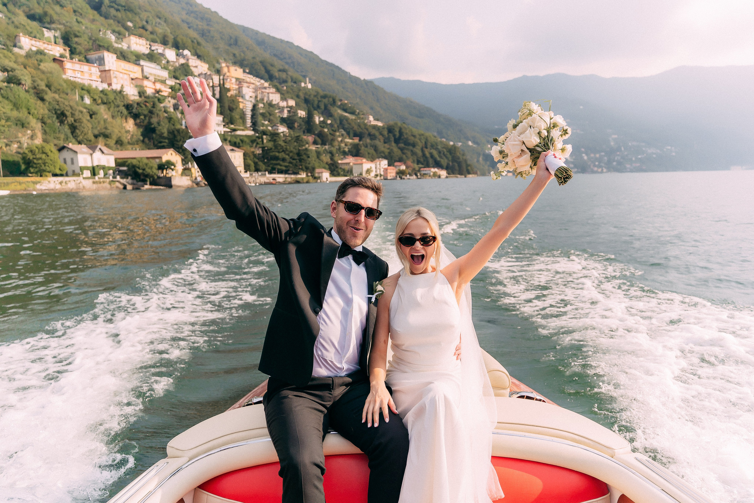 Bride and groom joyfully waving from the boat on Lake Como at Villa Lario, Italy