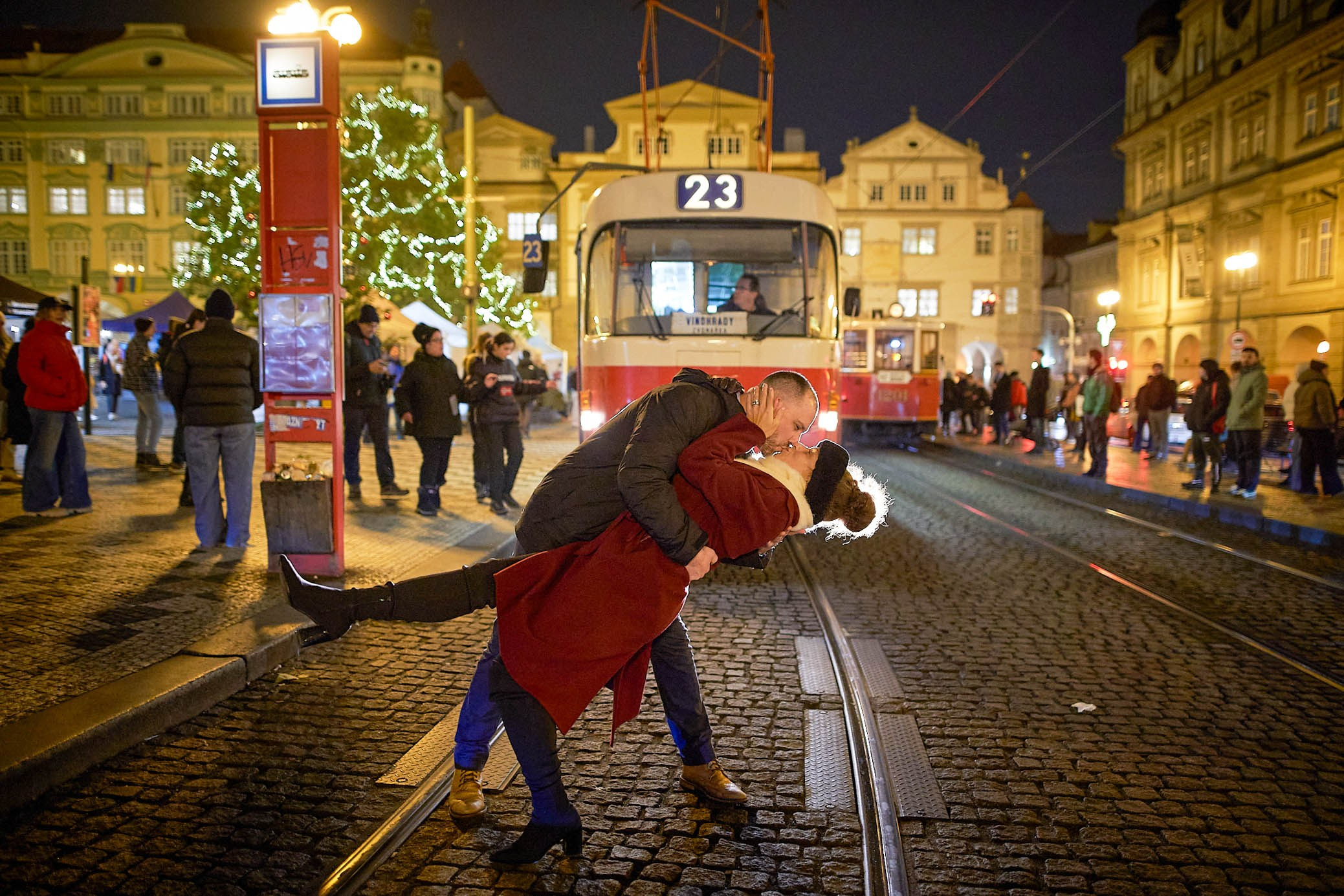 A man dips his partner and gives her a kiss in front of a tram in the Christmas themed Malostranske Namesty in the heart of Prague.