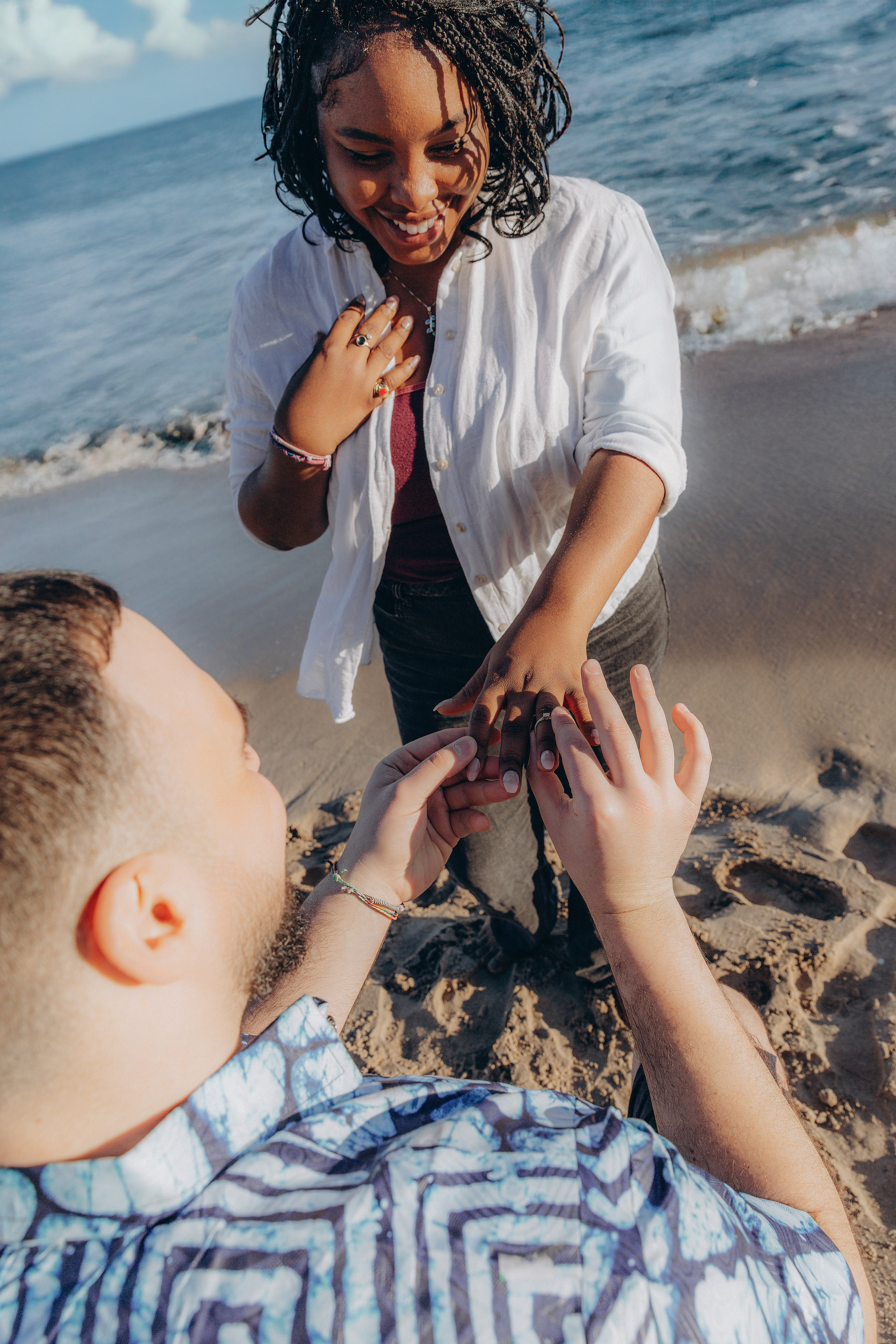 Propuesta alegre en la playa en Valencia, España — un momento espontáneo en el que un hombre pone el anillo de compromiso a su pareja mientras ella sonríe con felicidad. Ideal para quienes buscan sesiones emotivas y auténticas de propuesta en Valencia y en toda España.