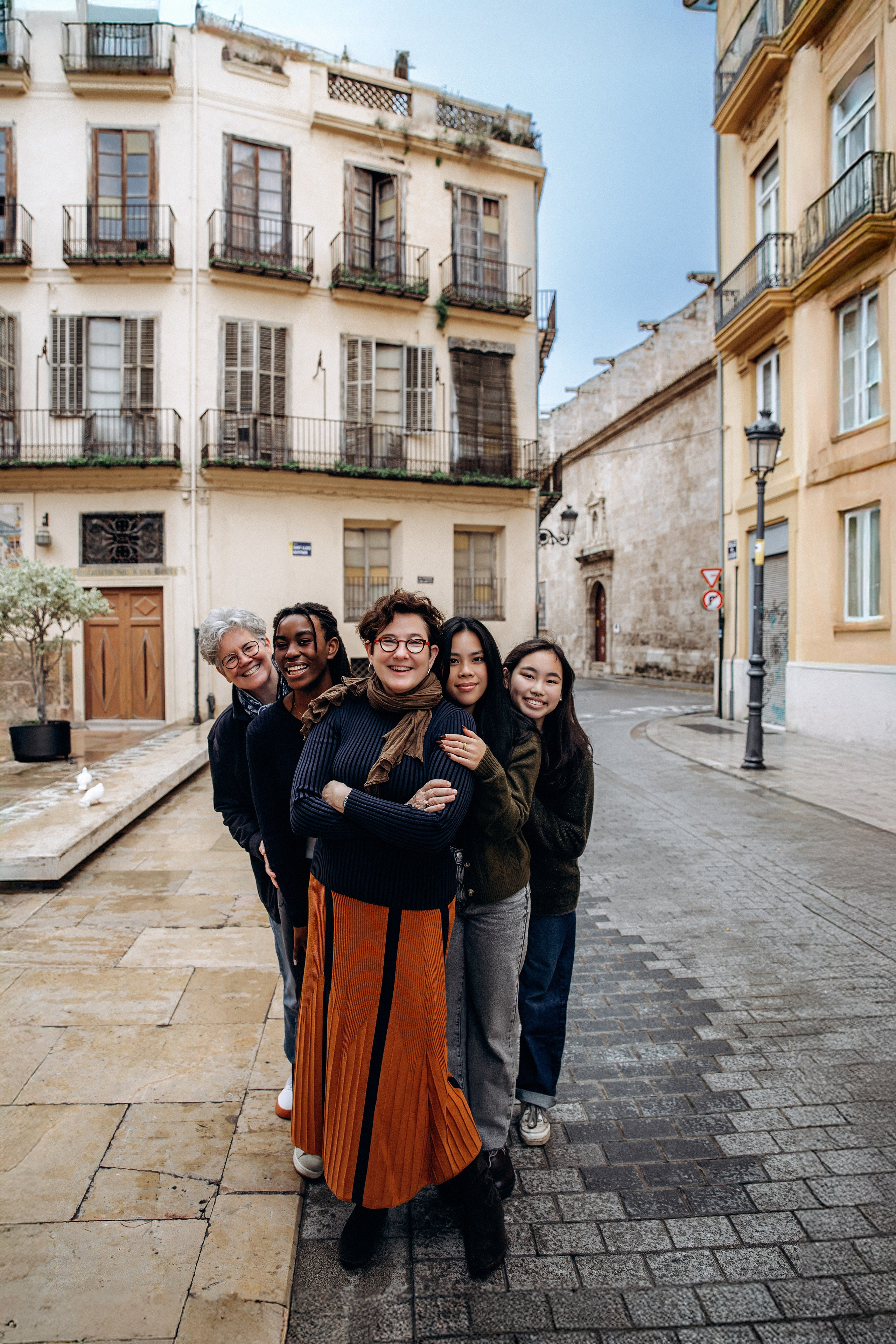 Семейная фотосессия в Валенсии, Испания, где группа членов семьи стоит вместе на живописной улице старого города со средиземноморской архитектурой, передавая тёплый и близкий семейный момент — идеально для семейных фотосессий в Валенсии и по всей Испании.