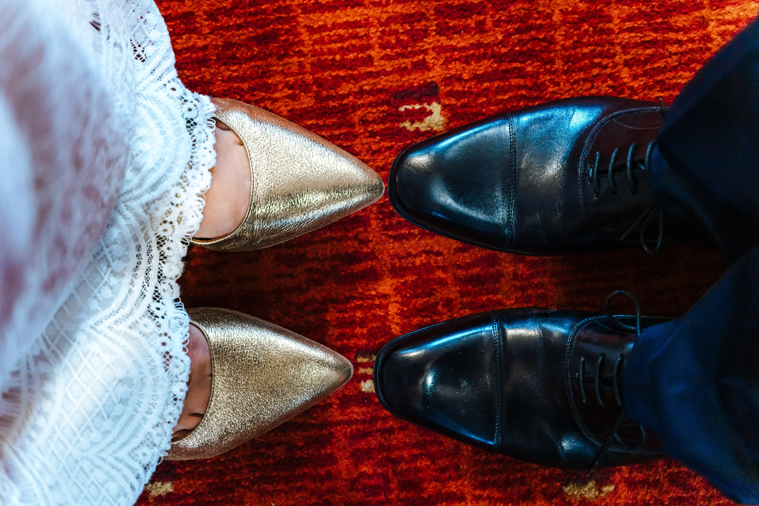 Close-up of the bride's white wedding shoes and the groom's navy shoes on the red carpet.