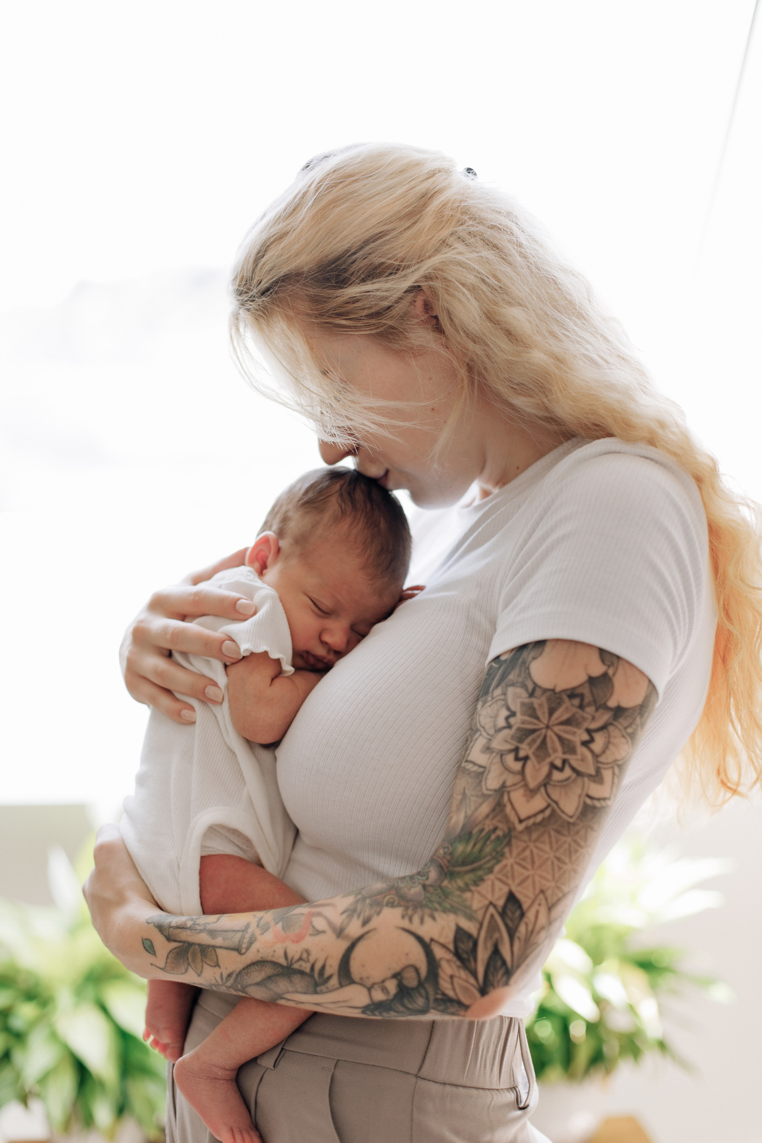 Baby kuschelt an die Brust der Mutter, die es sanft auf die Stirn küsst.