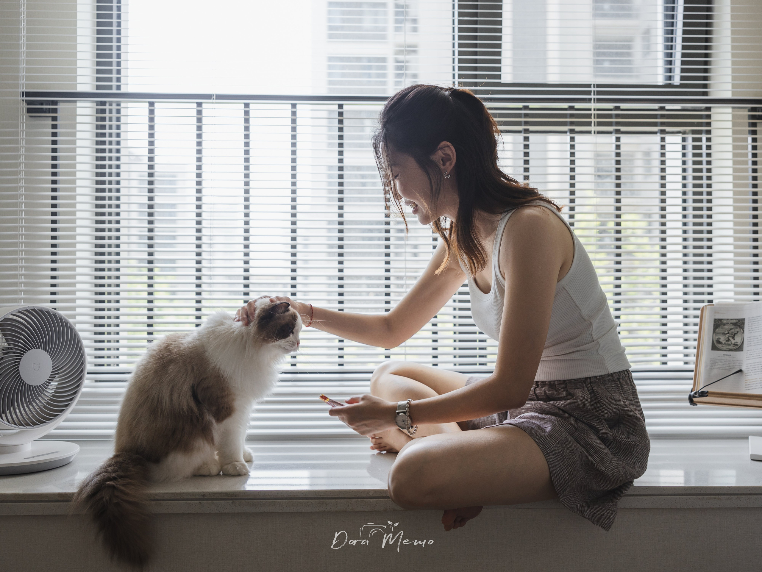 A woman sits on a windowsill gently petting her ragdoll cat under soft daylight — a cozy moment captured by a Shanghai lifestyle and pet photographer.